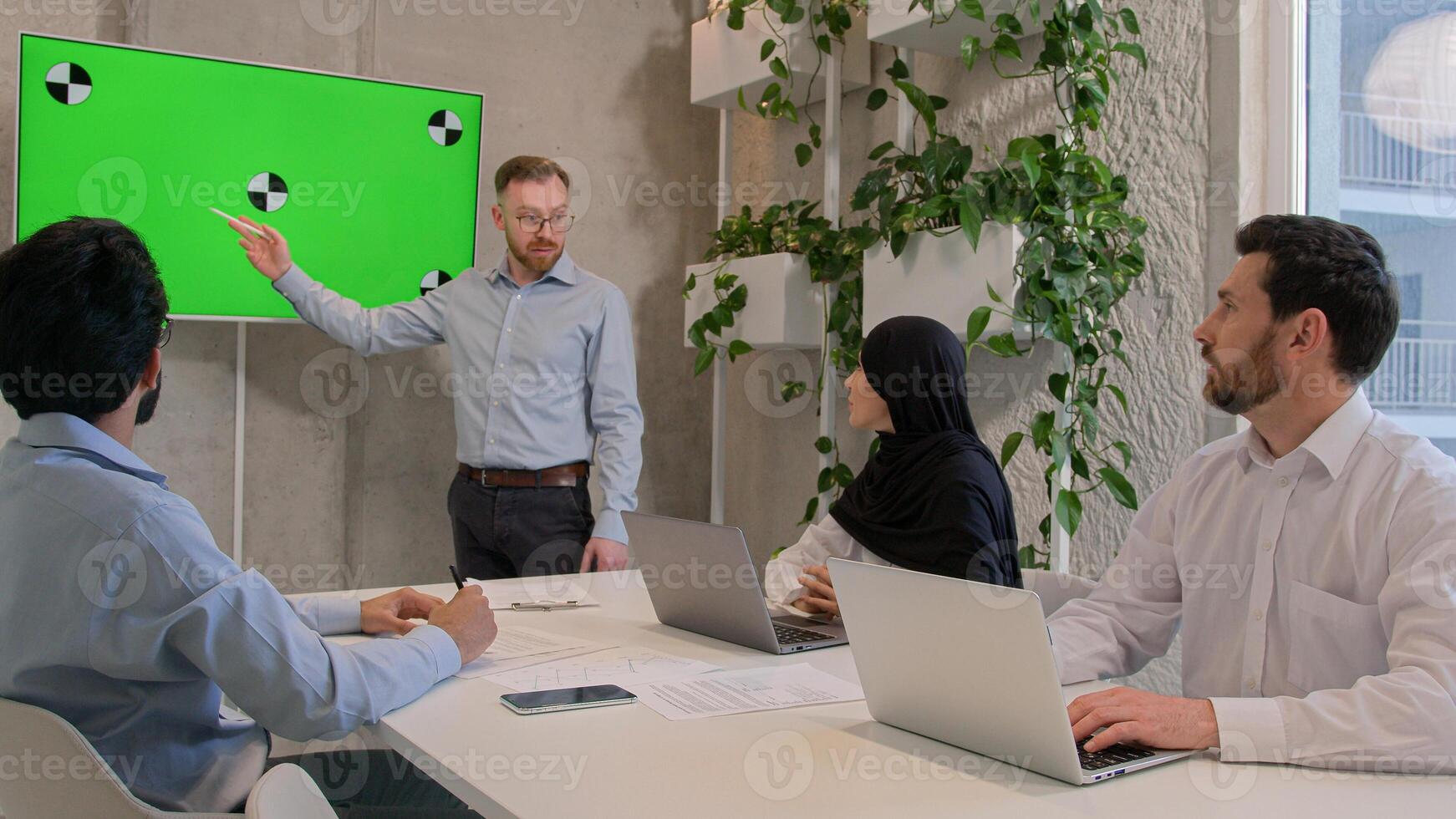 Office coworkers partners businessmen businesswoman looking on chroma key presentation at conference room male leader chief talking to diverse team showing green screen display business data analysis photo