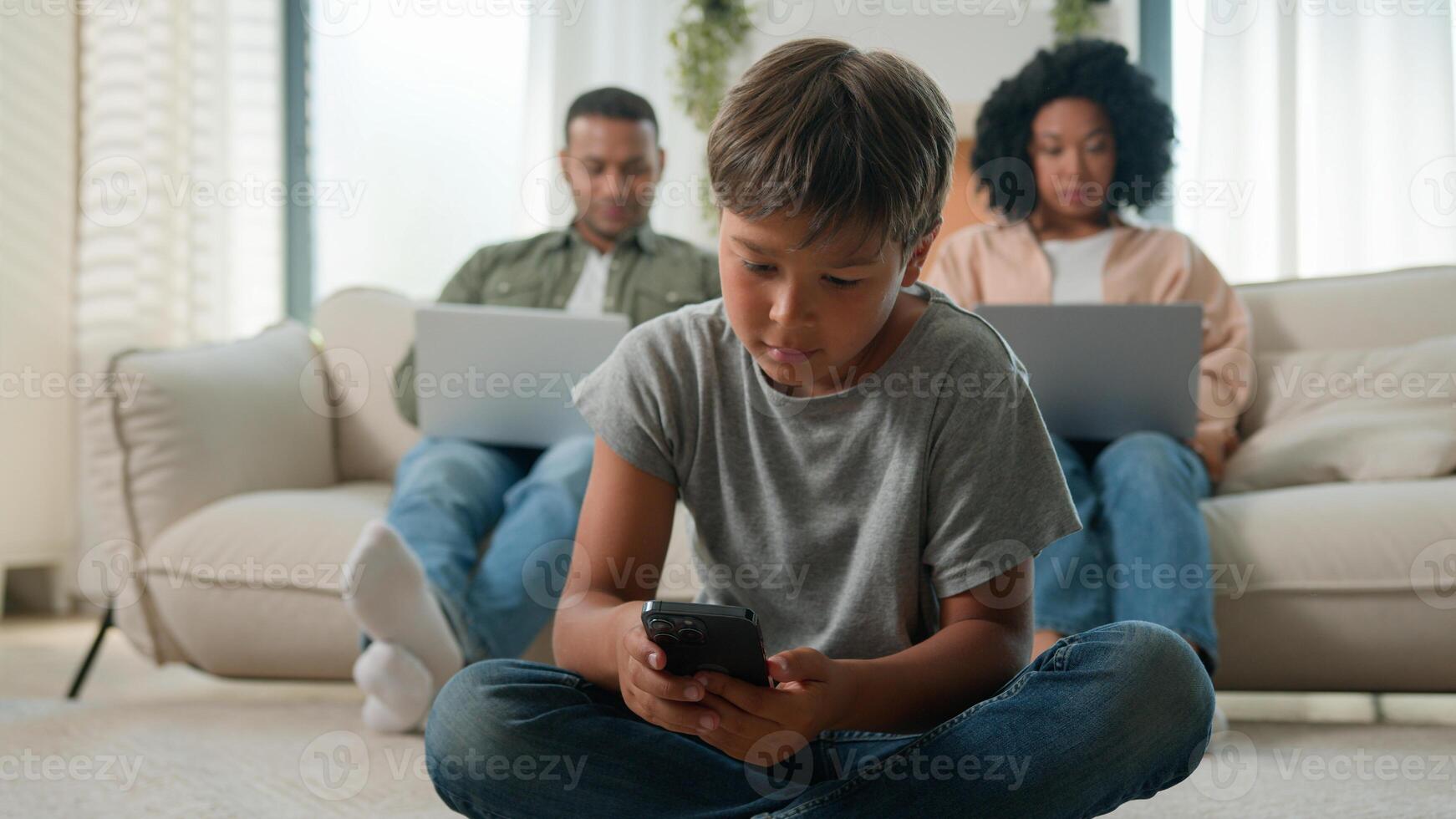 Modern gadgets addicted family using diverse devices at home African American multiracial parents on couch working online with laptops together little boy kid son child play game on mobile phone photo