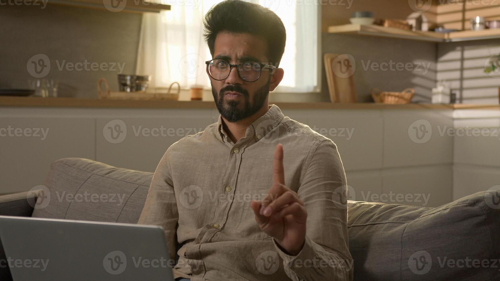 Arabian Indian man businessman freelancer working with laptop from home kitchen dissatisfied guy on sofa waving index finger negative warn sign no never warning gesture caution forbid disagree reject photo