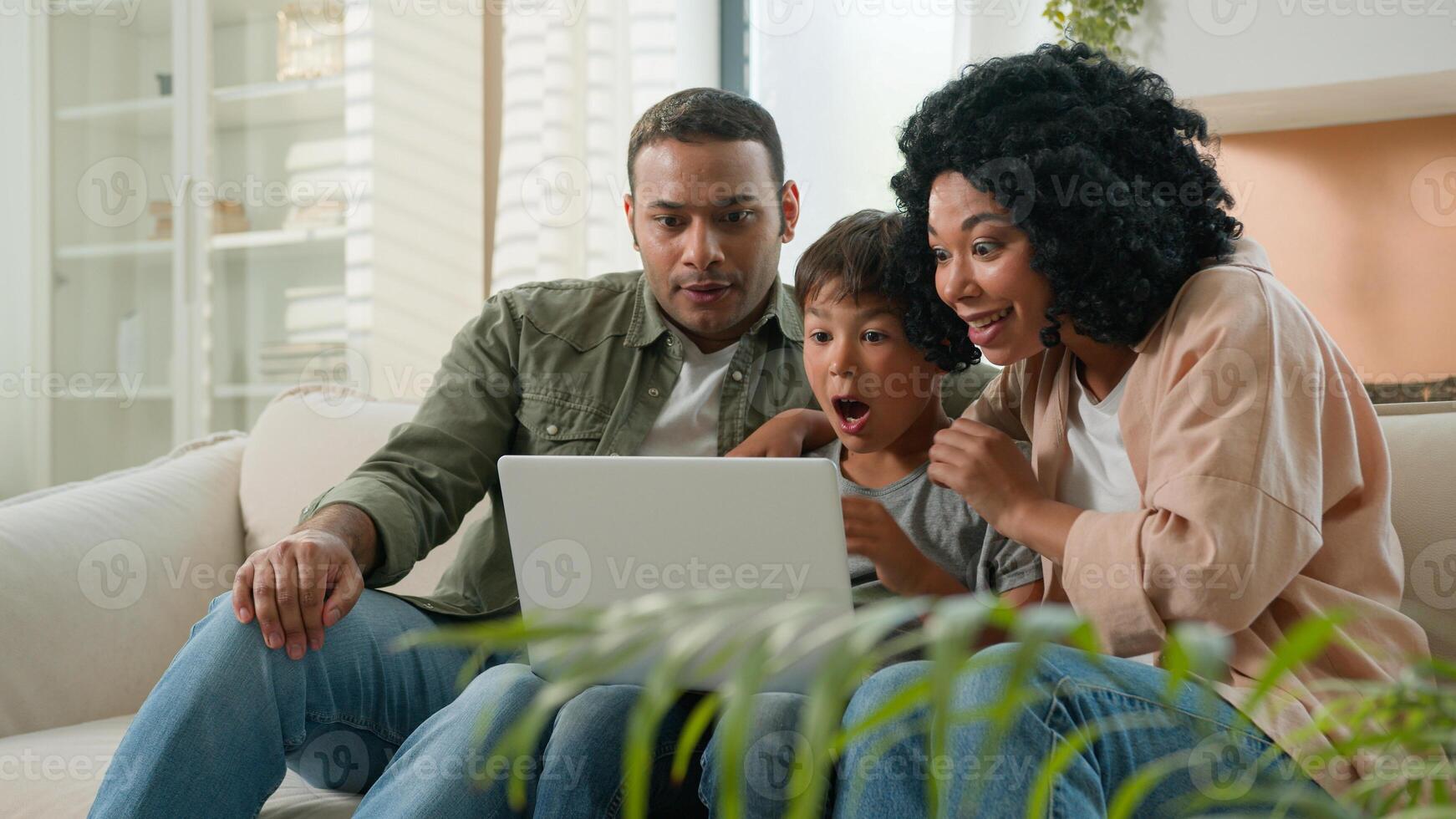 Home interior multiracial family parents child using laptop device together African American mother father and Caucasian little kid boy son winnning prize online lottery victory rejoice in apartment photo