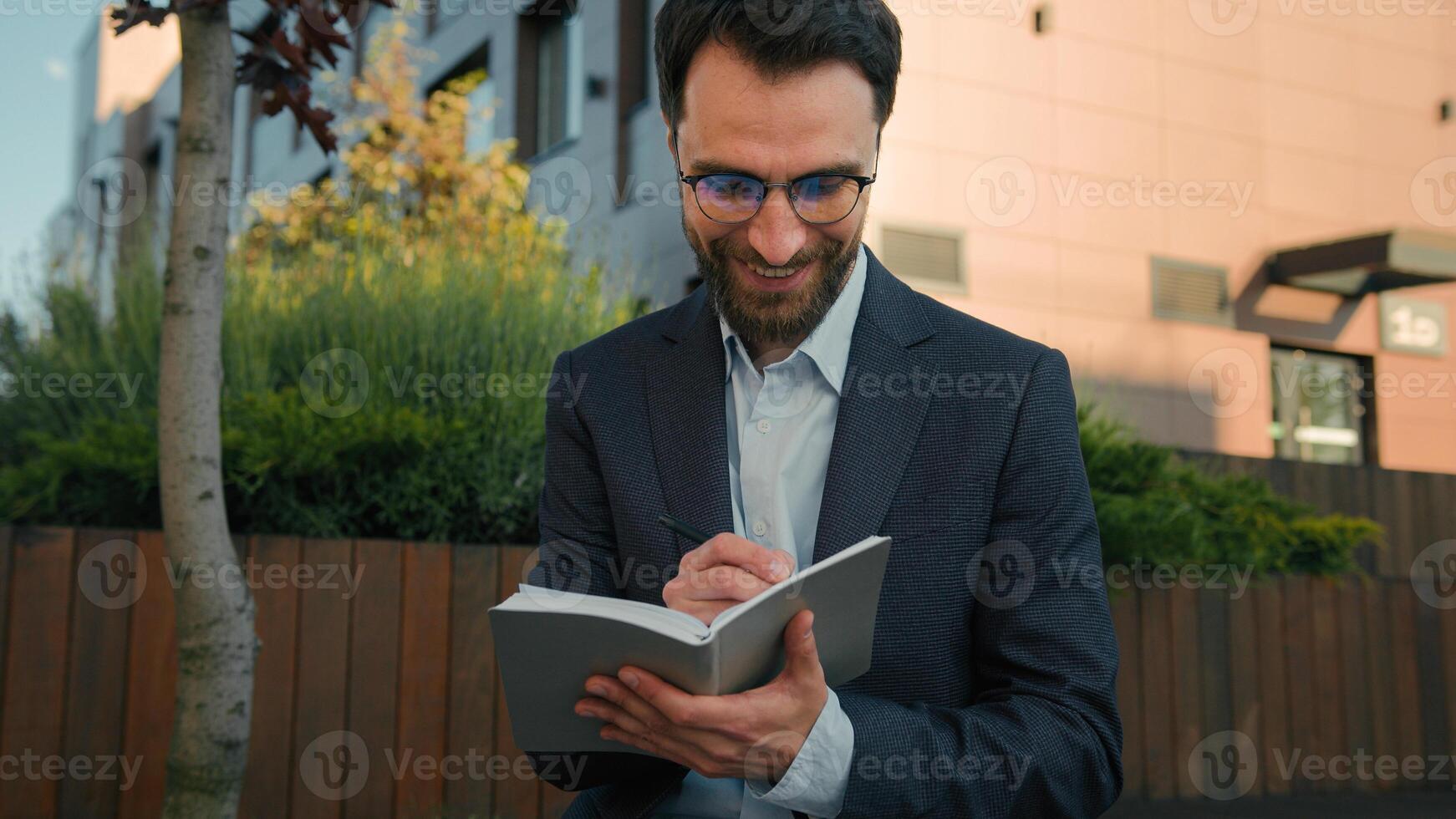 Caucasian business man businessman outside thinking writing notes in notebook university teacher professor in city hold paper notepad smile come up with idea creative thought prepare for exam studying photo