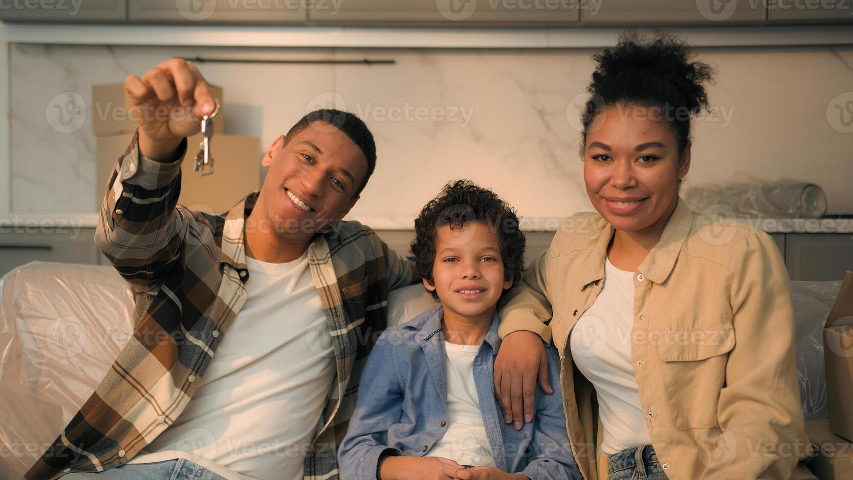 African American family buy house parents little son boy child kid together on couch happy home owners smiling at camera showing keys rent flat relocation moving day bank credit real estate mortgage photo