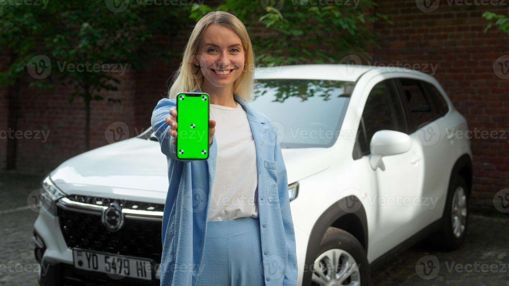 Cheerful satisfied Caucasian woman buyer girl businesswoman driver smile holding mobile phone automobile client female demonstrate green screen display in city auto service application rent online car photo