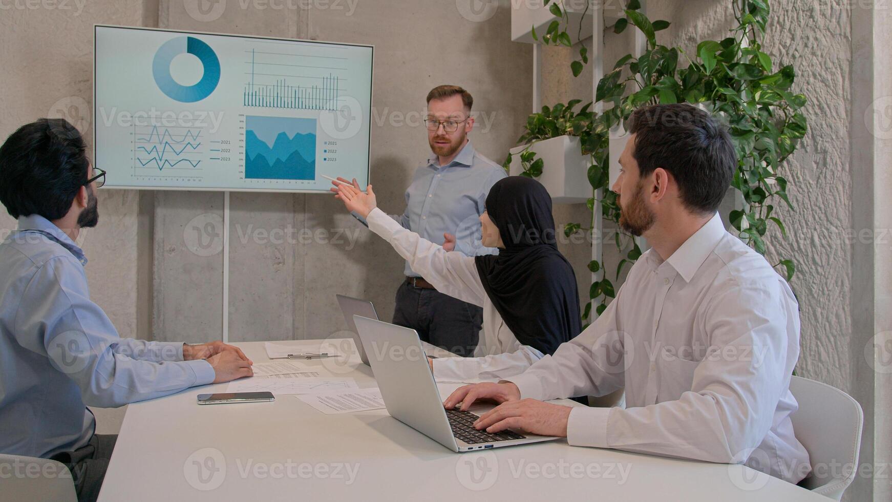 Office team leader man mentor show charts financial growth graphics presentation on interactive board diverse businessmen and muslim businesswoman in hijab discussing project group conference meeting photo