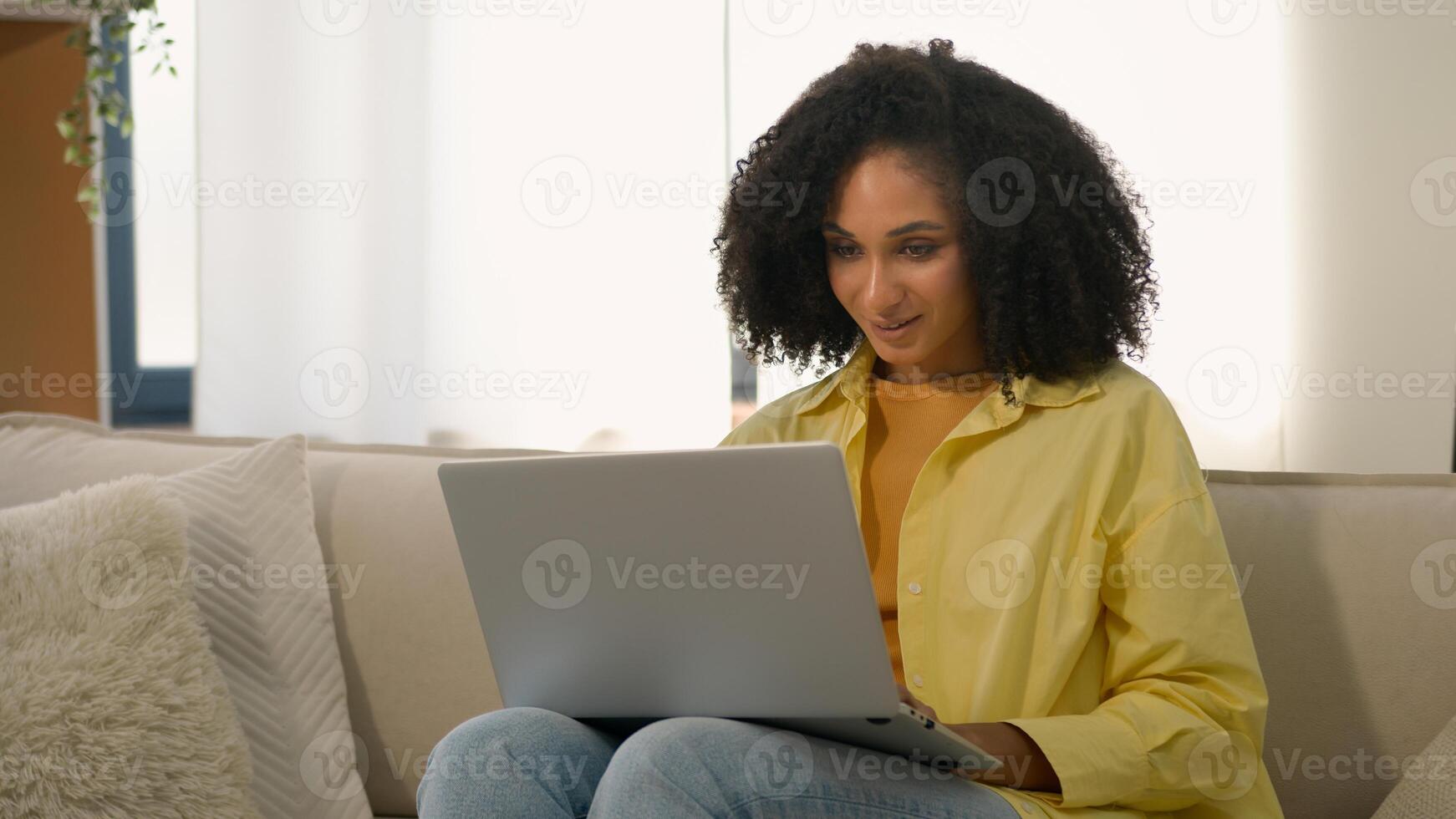 African American woman homeowner relaxing on couch with laptop device online chatting web surfing internet studying with computer at home ethnic girl businesswoman freelance business work e-learning photo