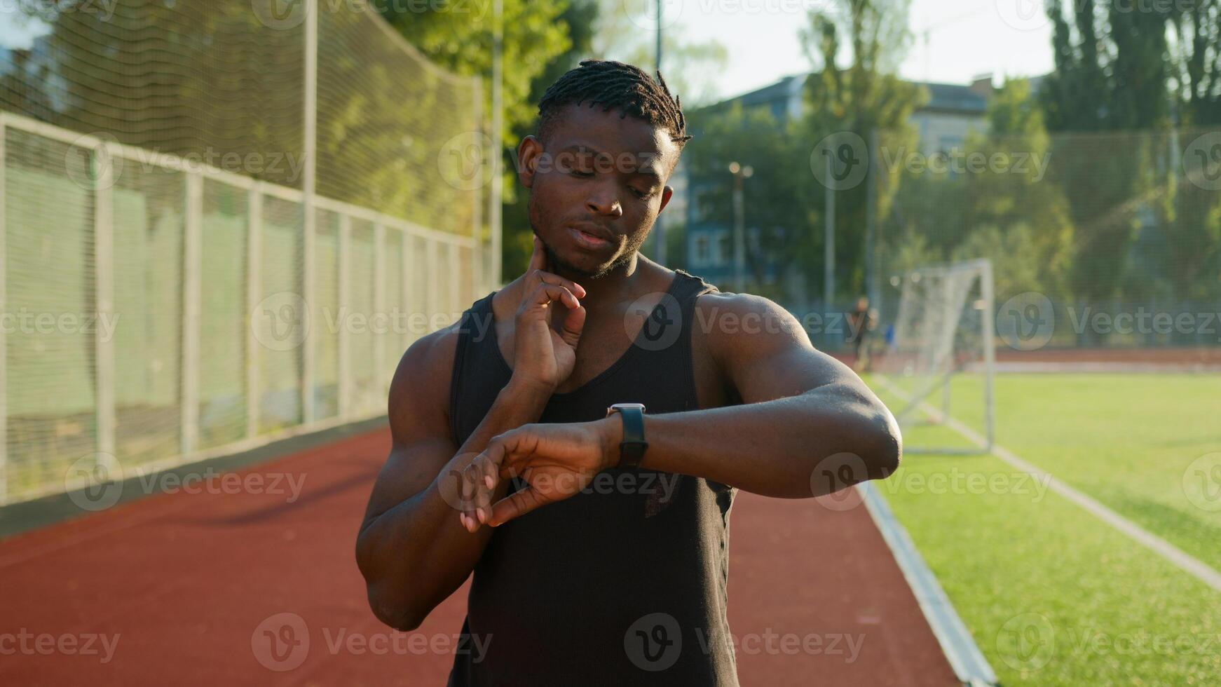 African American man runner jogger athlete muscular sportsman training outdoors athletic ethnic guy using smart band checking neck pulse heart rate result on smartwatch before running on sport stadium photo