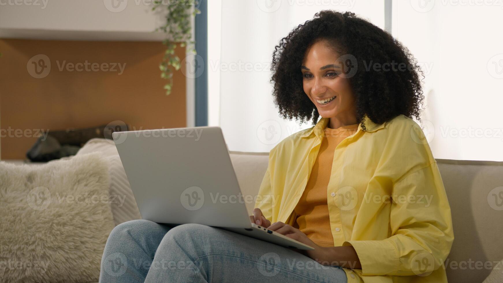 African American woman homeowner relaxing on couch with laptop device online chatting web surfing internet studying with computer at home ethnic girl businesswoman freelance business work e-learning photo