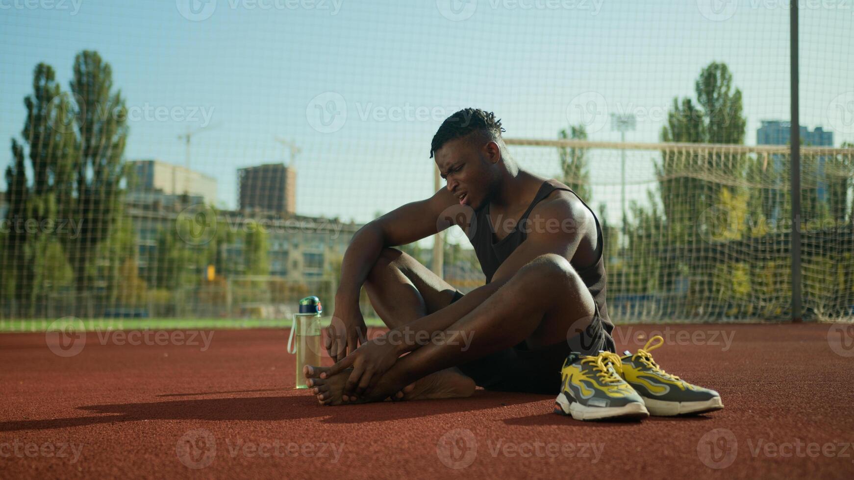 African American footballer sportsman sit on field suffer pain sharp ache muscle cramp foot injury sporty man injuring leg in training outside sport trauma damage feet painful joint workout outdoors photo