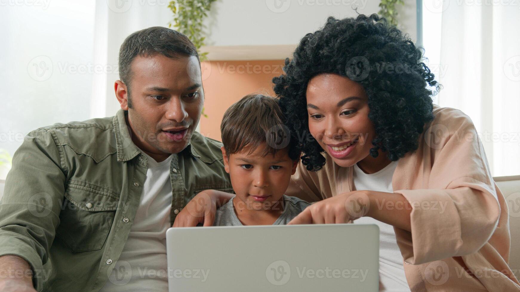 Multiracial family happy mom dad son looking at laptop together African American parents mother father and adopted Caucasian little son boy child kid win success rejoice victory emotion wonder at home photo
