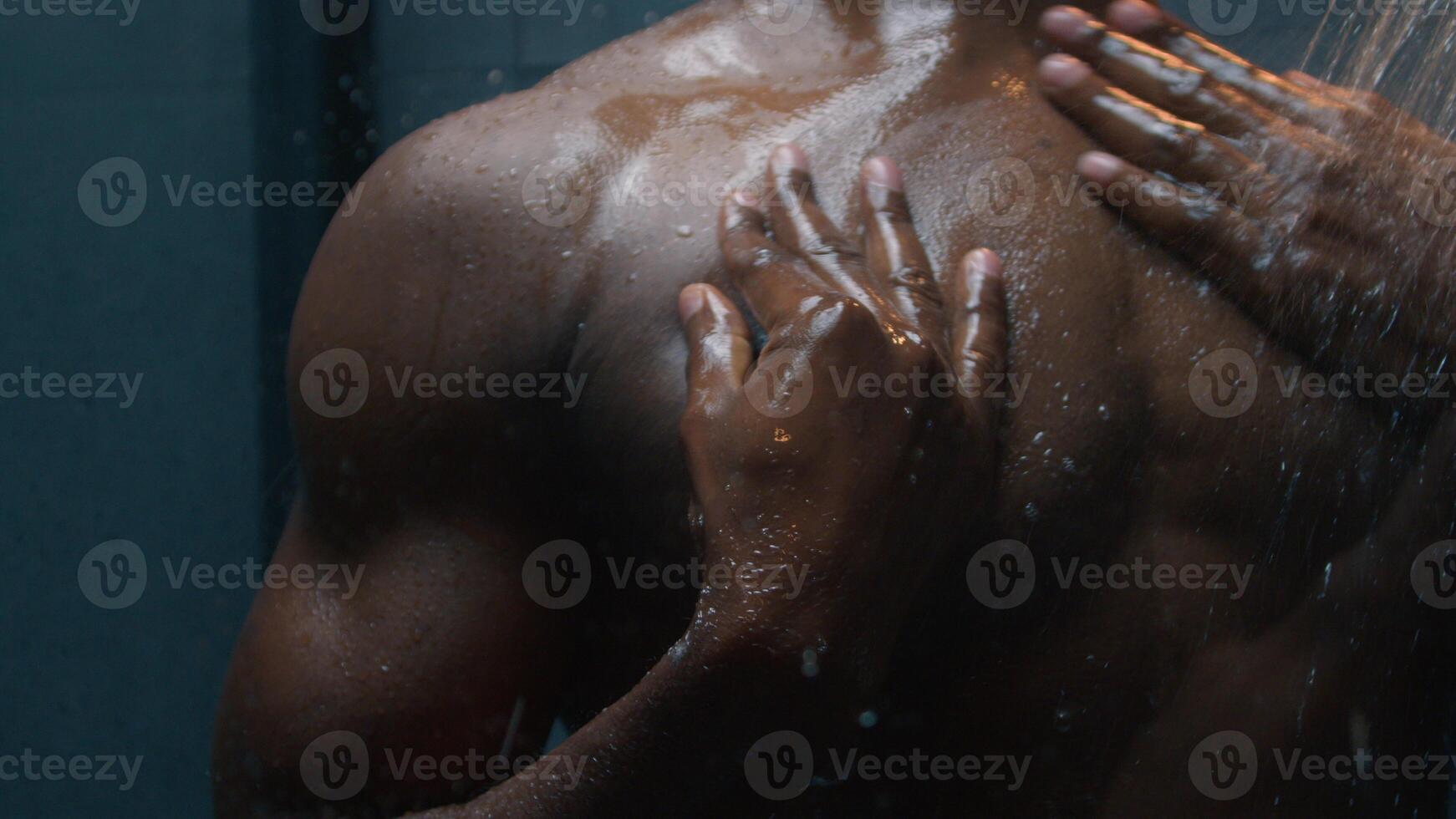 African American naked sexy ethnic man bare wet guy washing body applying shower gel shampoo liquid soap rinsing foam under hot water clean skin bathe hygiene male beauty bath cosmetics advertising photo