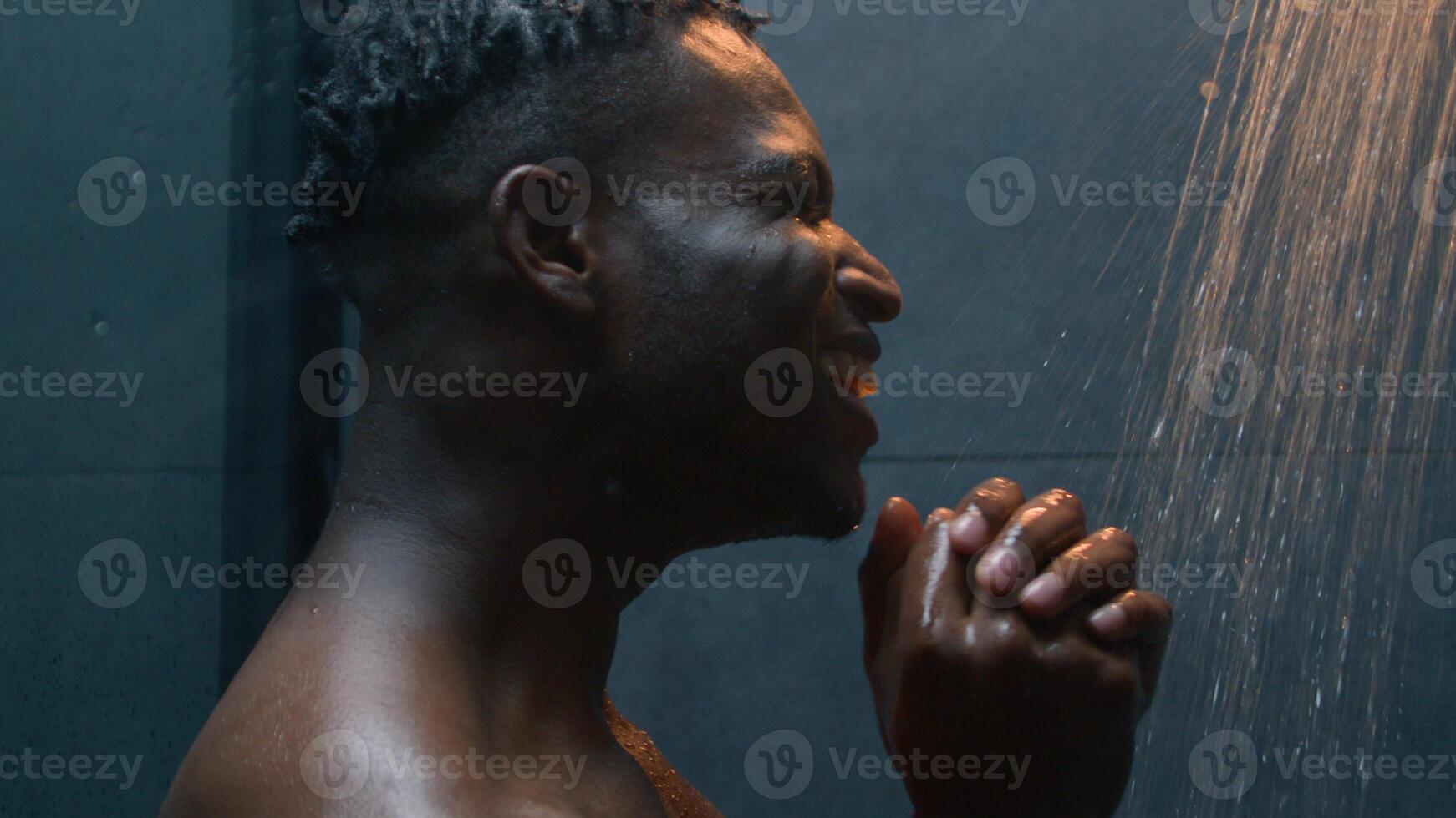 Close up African American man happy ethnic millennial guy singing favorite song in shower enjoying morning hygiene hot water washing relaxing dancing naked joyful carefree male sing in bath body clean photo