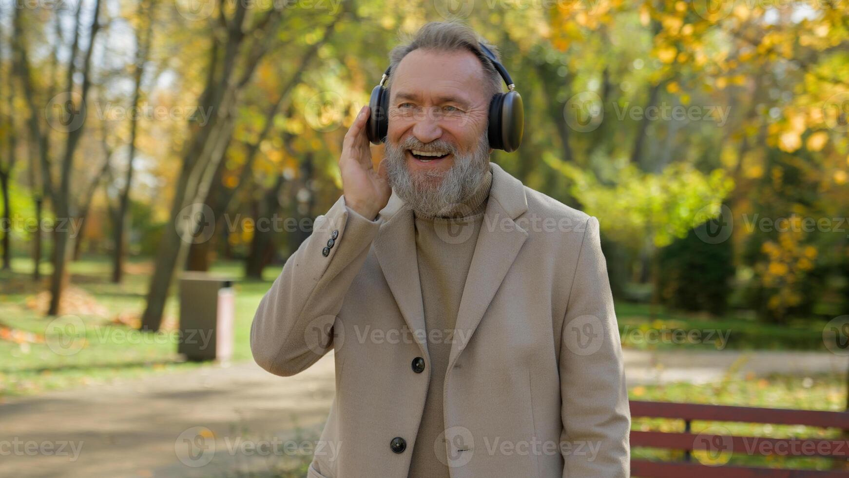 Happy carefree joyful old man Caucasian male senior middle aged mature retired businessman listen music in wireless headphones earphones in city enjoy song smile relax dance weekend in park outdoors photo