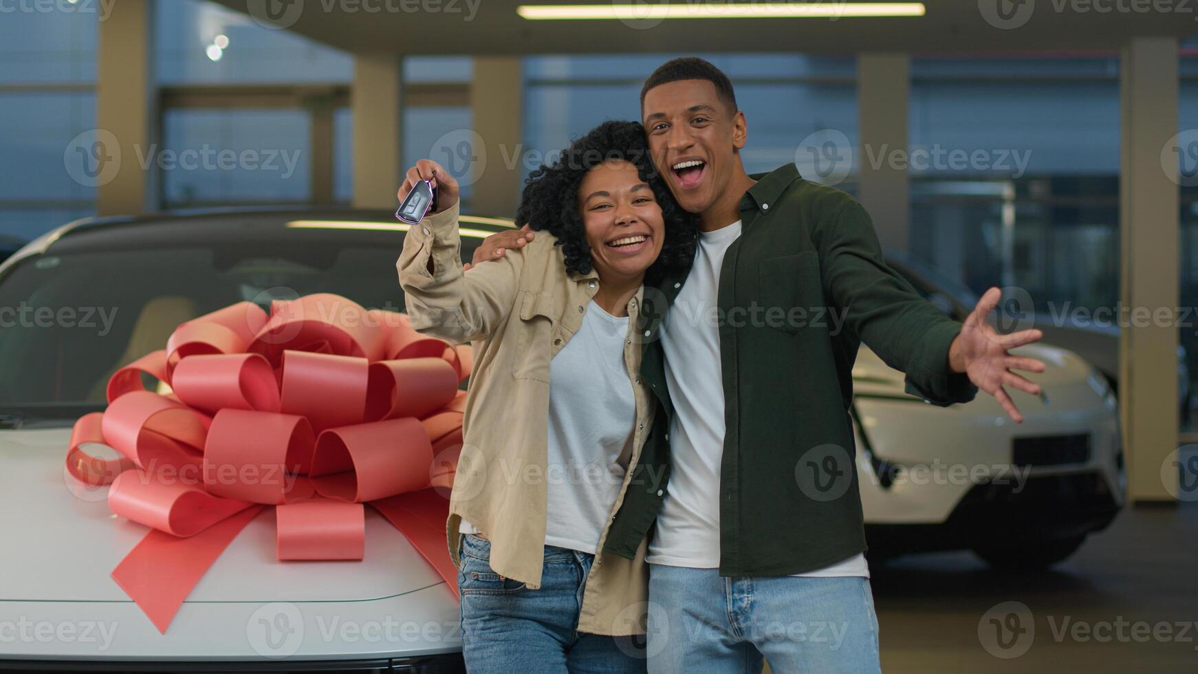 Happy smiling couple African American family woman man new car owners buyers showing keys at camera buying automobile with big bow at dealership store excited joyful male female buy luxury auto credit photo