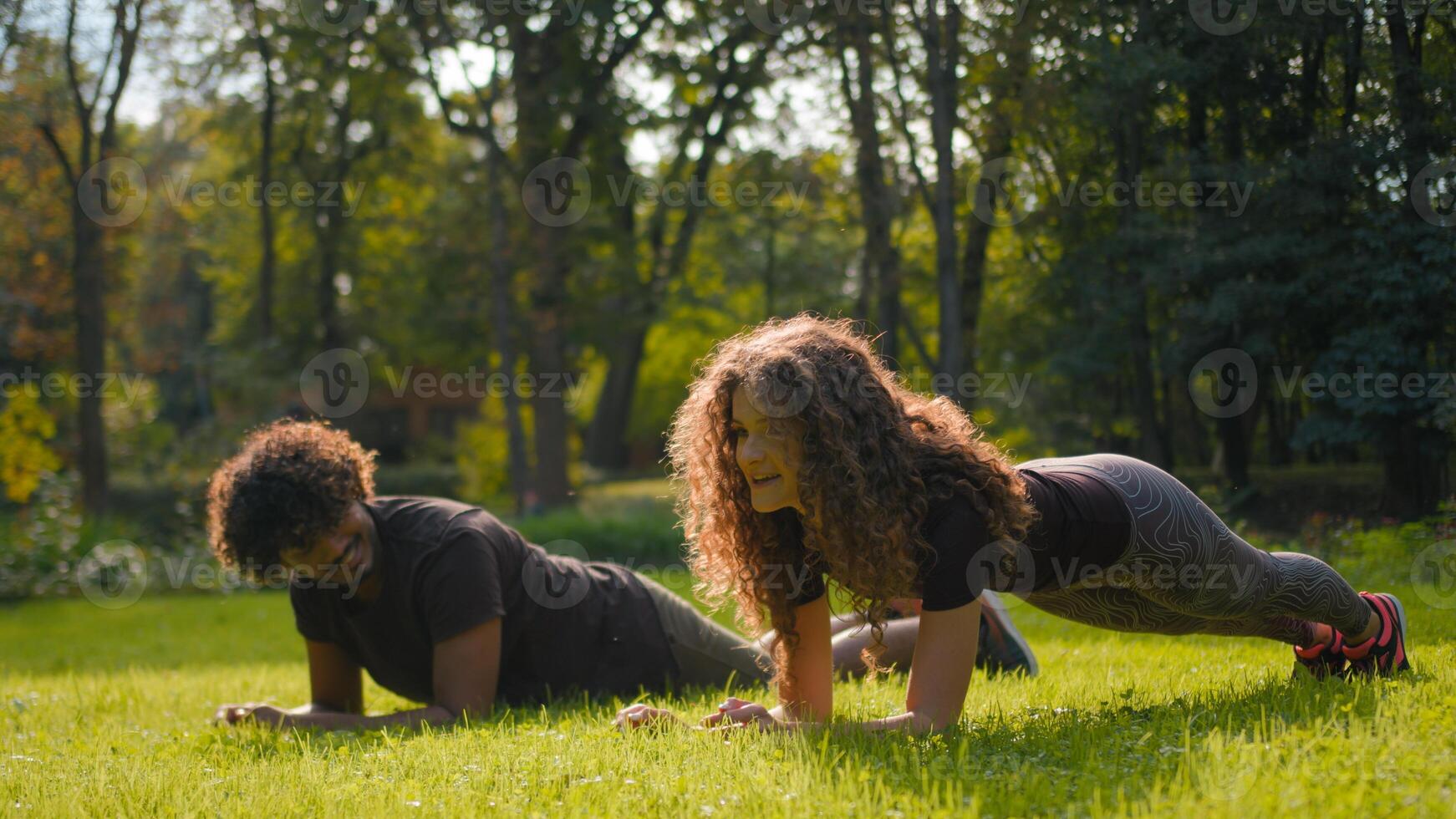 Indian Arabian man and Caucasian woman fitness couple planking on yoga mat together in city park sporty male female friends athletes strength training sport exercise healthy lifestyle workout outdoors photo