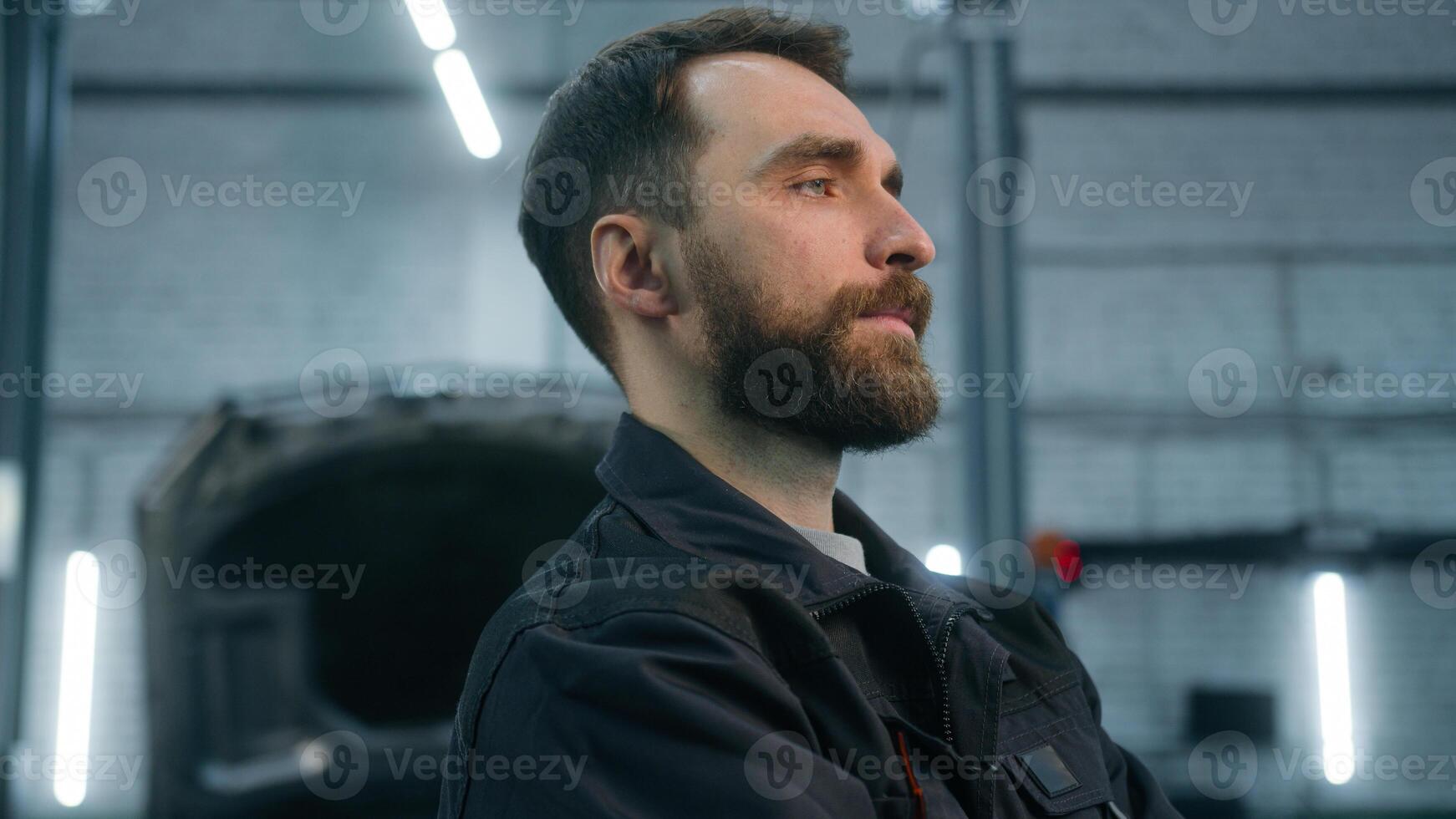 Close up male portrait Caucasian man professional industrial worker in uniform mechanic auto engineer technician specialist guy serious looking profile posing with crossed hands in car service factory photo