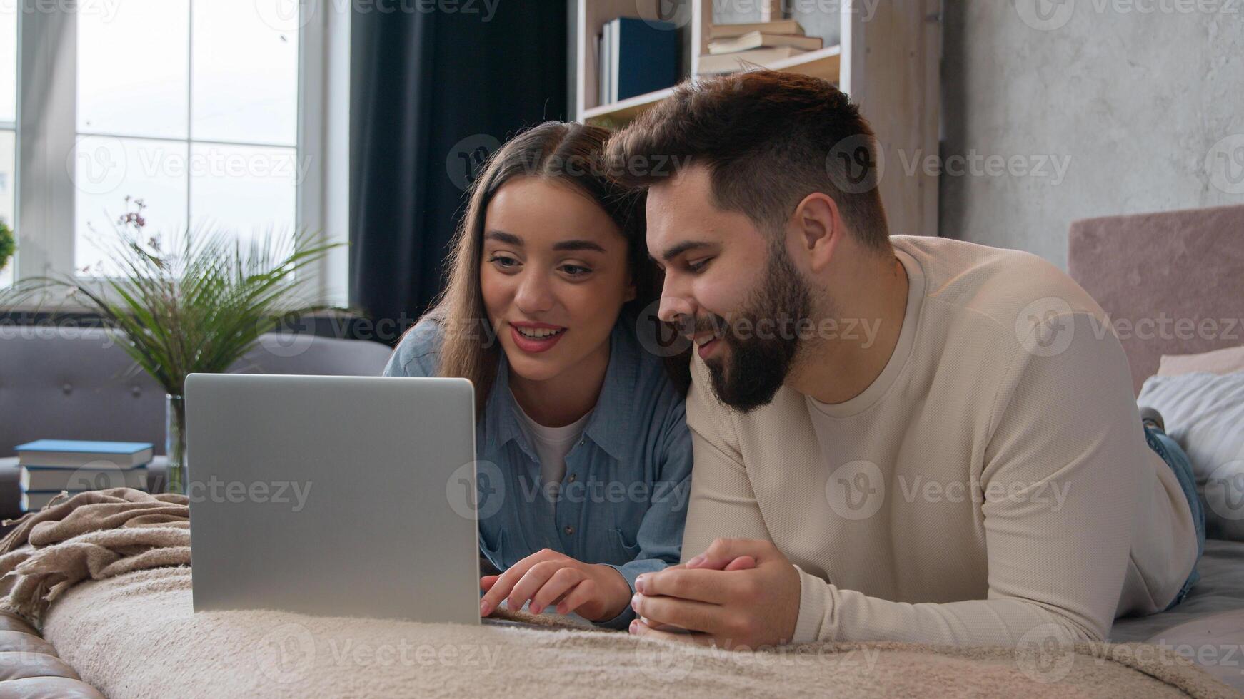 Caucasian family couple in love woman wife and man husband shopping online with laptop computer on cozy bed smiling boyfriend and girlfriend booking tickets buy internet order e-commerce talk together photo