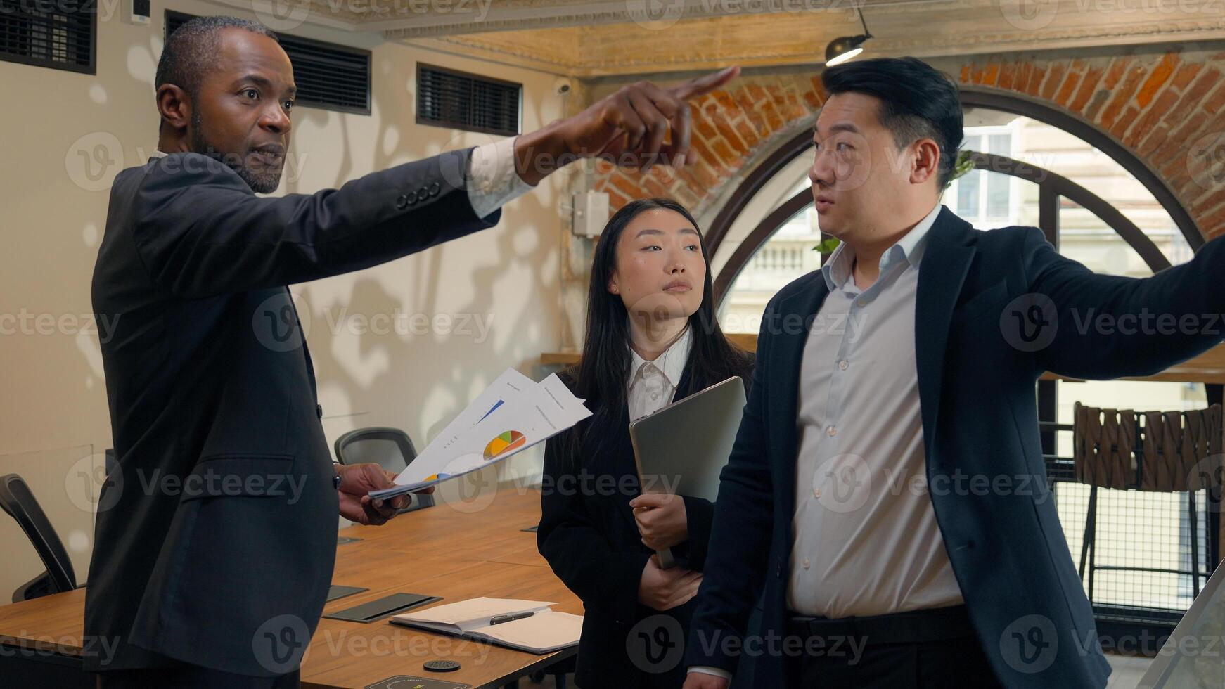 Three multiracial business colleagues coworkers multiethnic in office Asian woman businesswoman Korean Japanese Chinese men businessmen African boss leader talk document discuss pointing data diagram photo