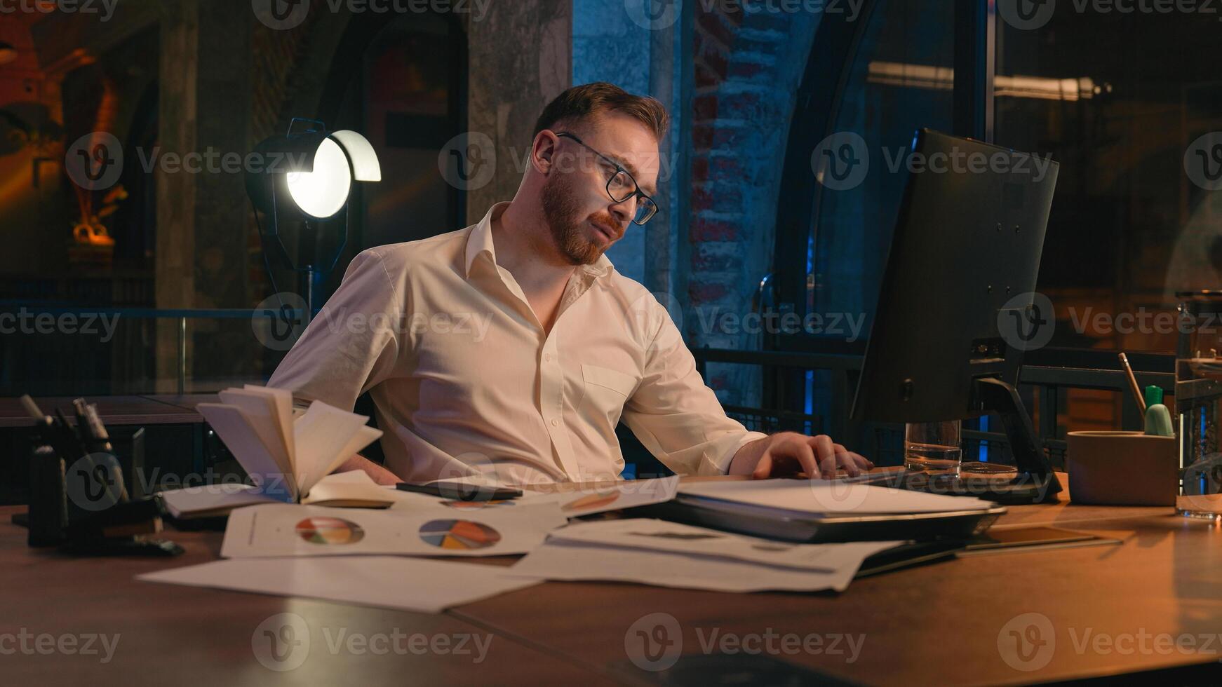 Caucasian man business guy businessman male workaholic in dark night office overworked overtime tired exhausted yawning low energy late time need sleep deadline working computer yawn health insomnia photo