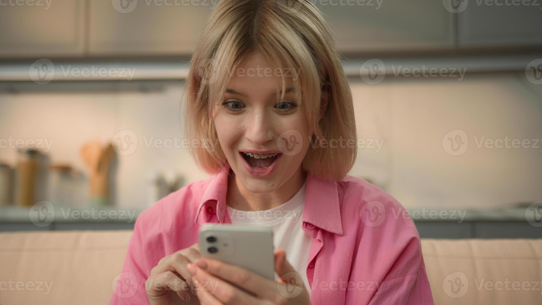 Emotional happy excited amazed wonder Caucasian girl woman female win cellphone money prize discount cashback victory amazing good news homeowner lady at home winning mobile phone achieve success luck photo