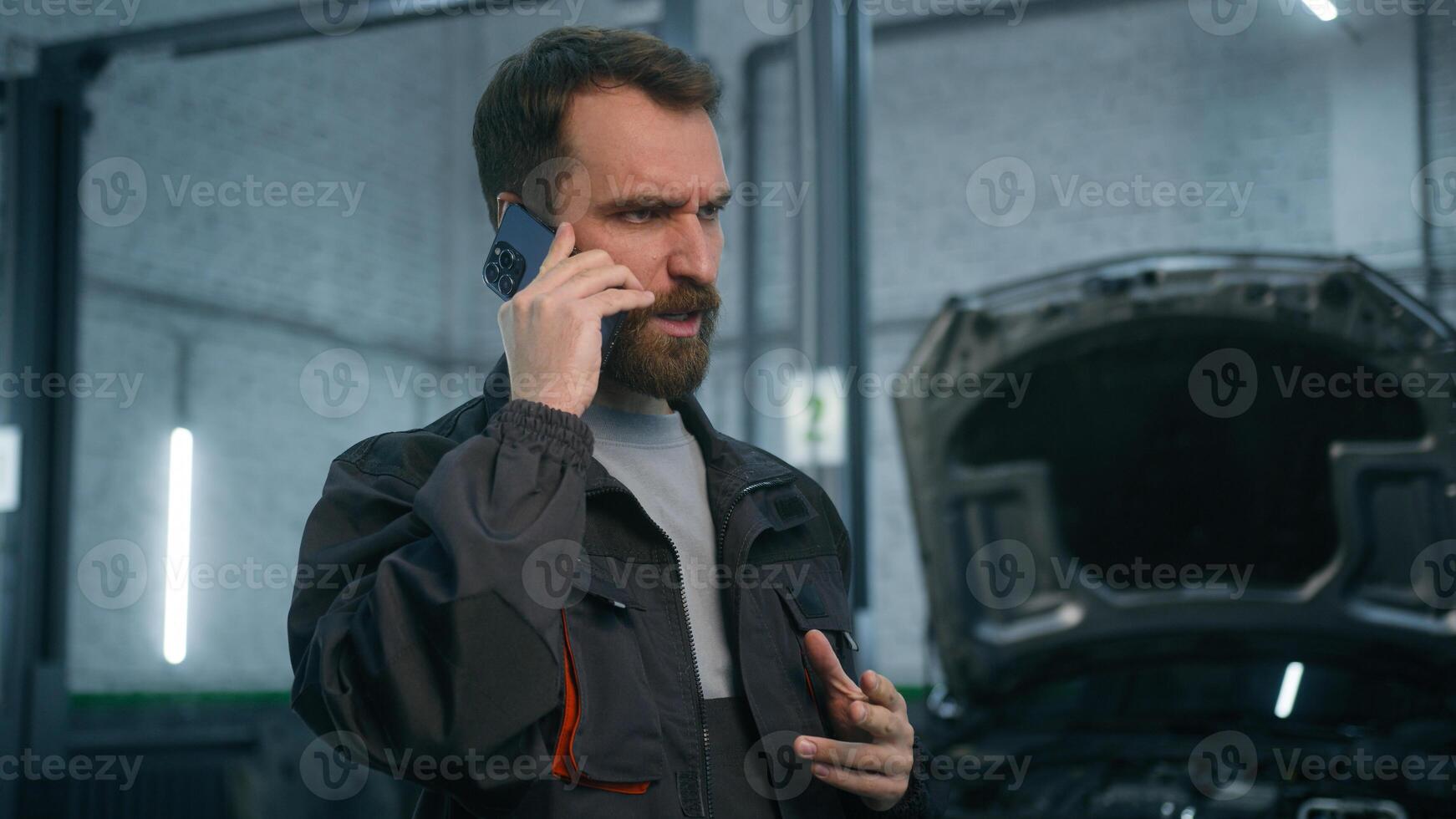 Anxious upset guy Caucasian man auto repairman service manager talking mobile phone in workshop station male worker automobile mechanic talk to client explain car problem transport vehicle breakdown photo