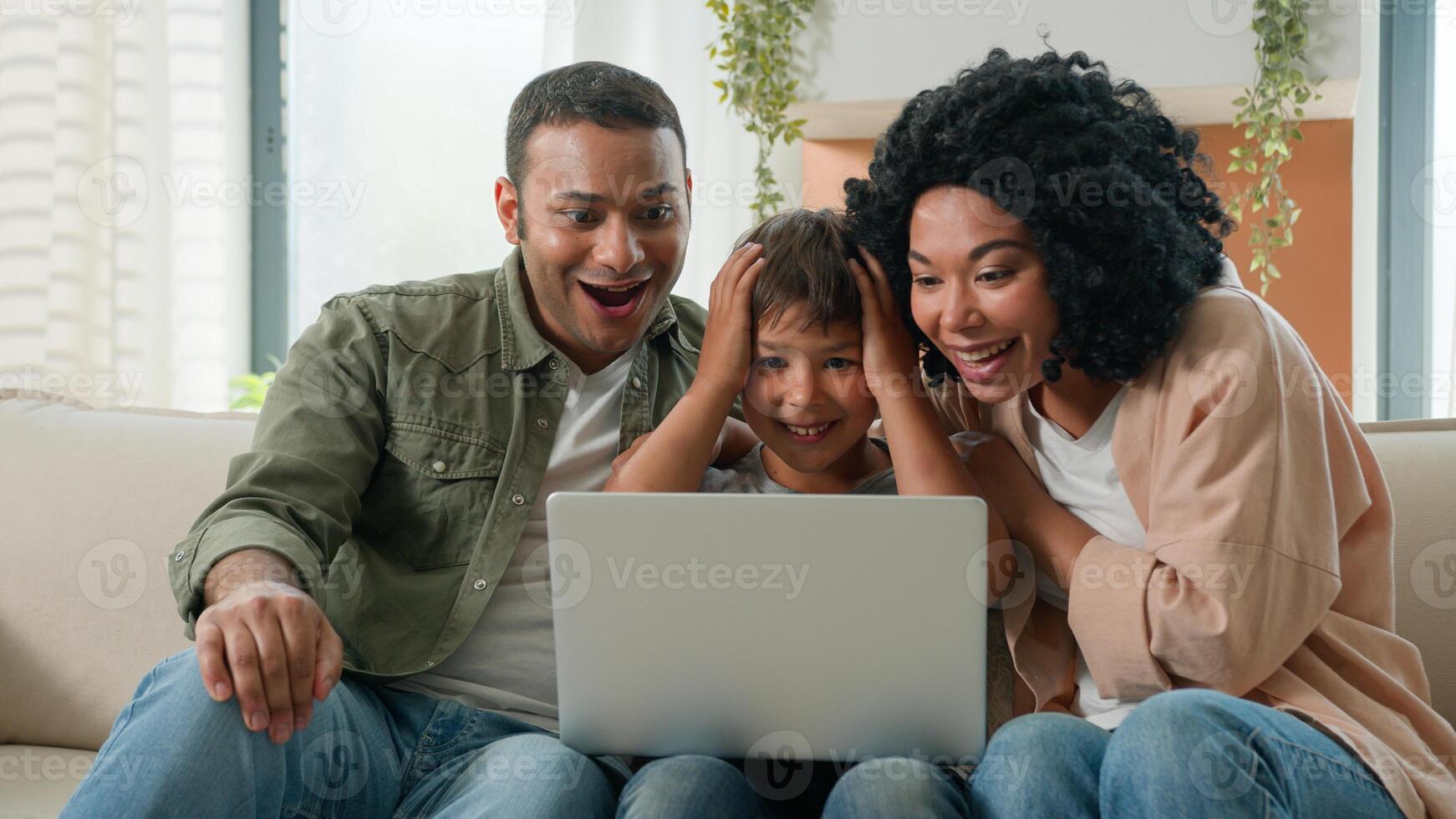 Home interior multiracial family parents child using laptop device together African American mother father and Caucasian little kid boy son winnning prize online lottery victory rejoice in apartment photo