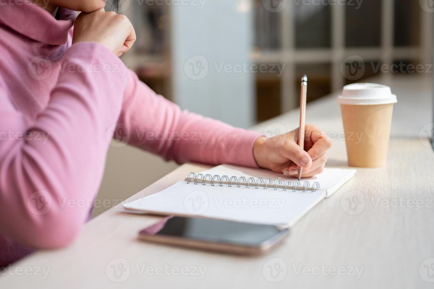A close-up of a woman deep in thought, as she writes in her diary while sitting in a coffee shop. photo