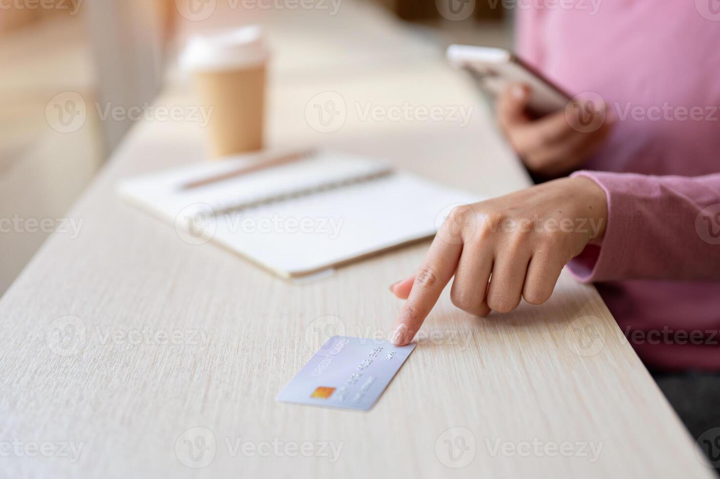 A woman sitting in a coffee shop, pointing at a credit card on the table. photo