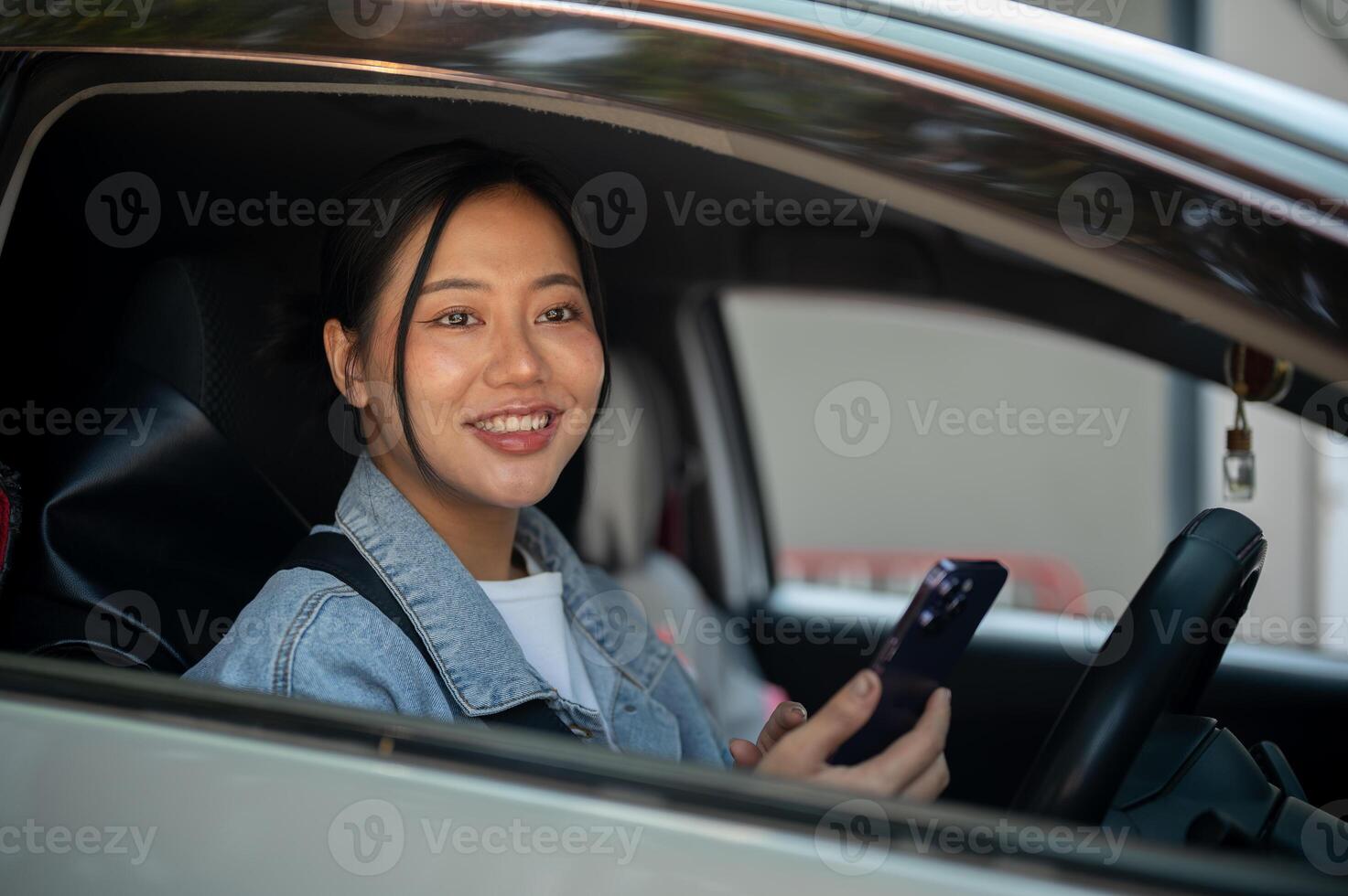 A positive Asian woman holding her smartphone while driving. photo