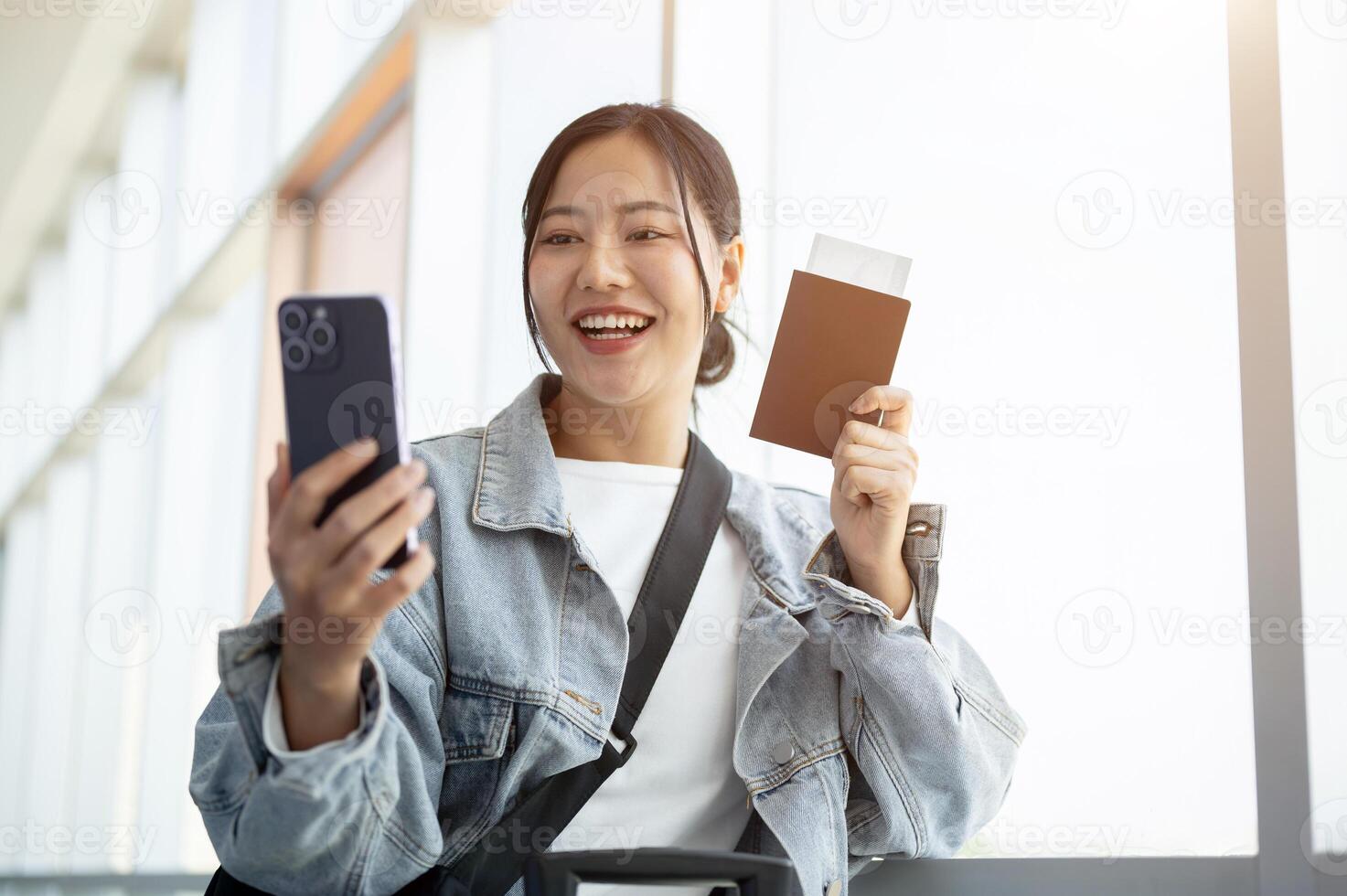A cheerful Asian female passenger enjoys talking on a call while waiting for her flight. photo