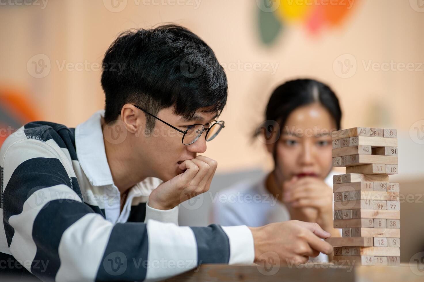 A happy young Asian man enjoys playing Jenga wooden blacks with his friends at home. photo
