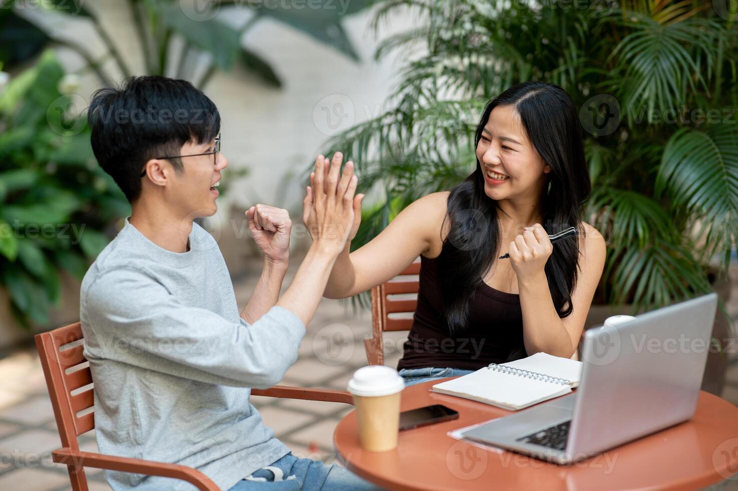 Cheerful Asian woman gives a high five to her colleague during an informal meeting at a coffee shop. photo
