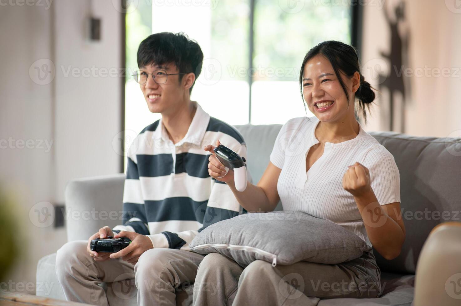 Two joyful Asian friends are enjoy playing a game on the sofa in the living room together. photo