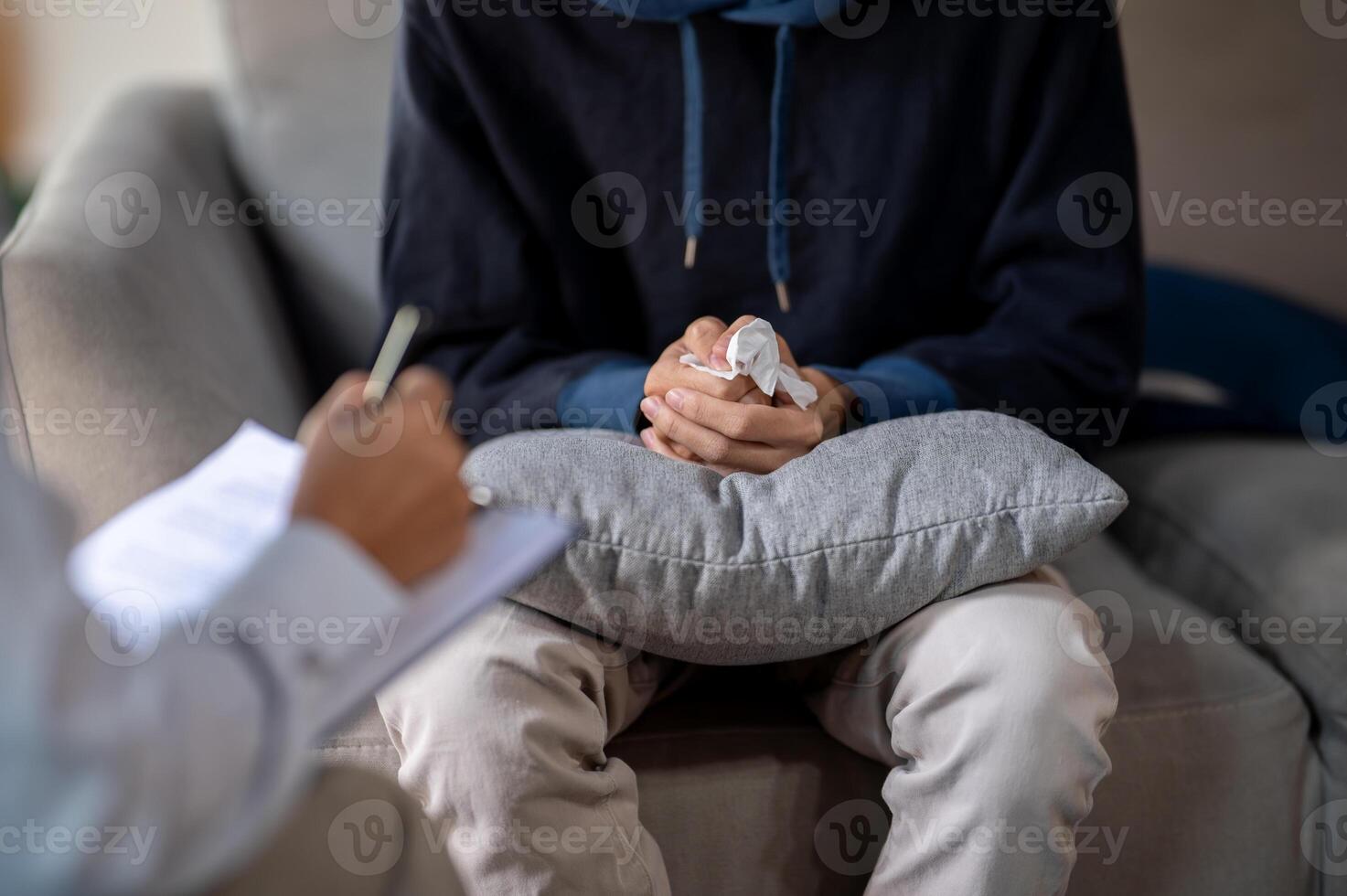 A stressed man sitting on a sofa, clasping his hands together during a mental health checkup. photo