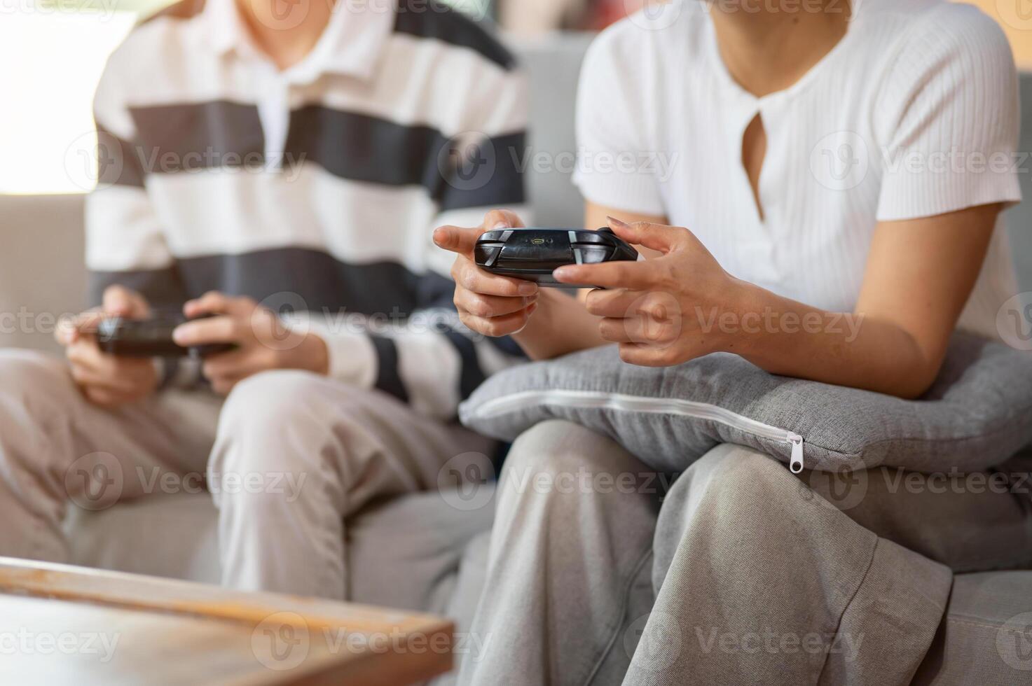 A close-up of two friends, a male and a female, play a game with joysticks on the sofa. photo
