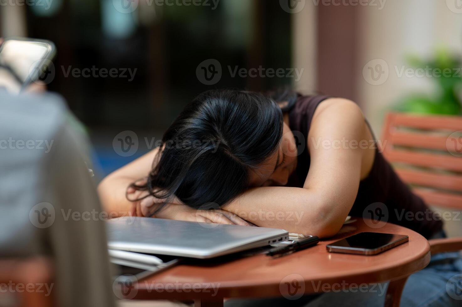 A tired, sleep-deprived Asian woman takes a nap at an outdoor table while working on her tasks. photo