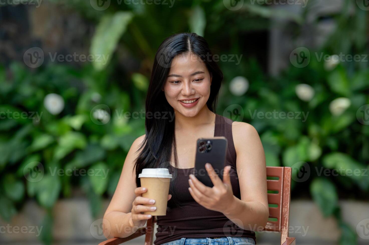 A beautiful Asian woman reads online news on her phone while enjoying coffee at an outdoor table. photo