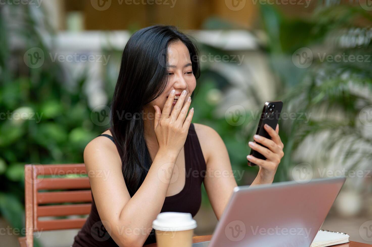 A beautiful Asian woman enjoys chatting on her smartphone while working remotely. photo
