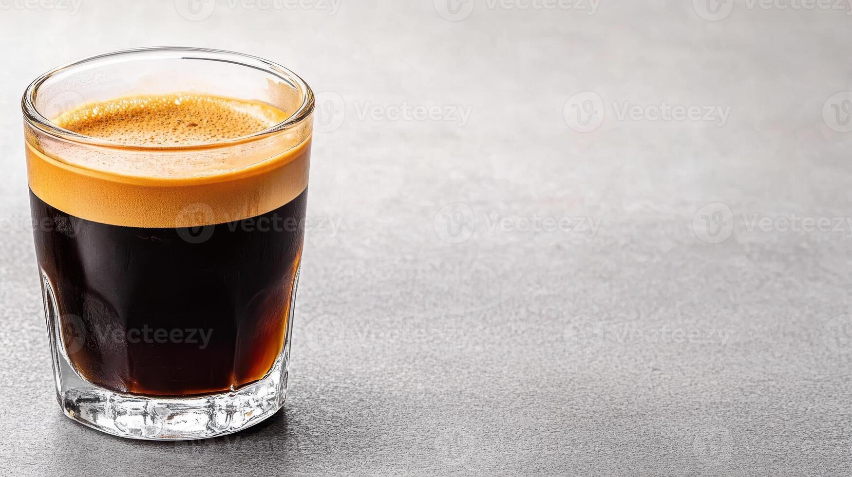 rich espresso with golden crema in glass on gray surface photo