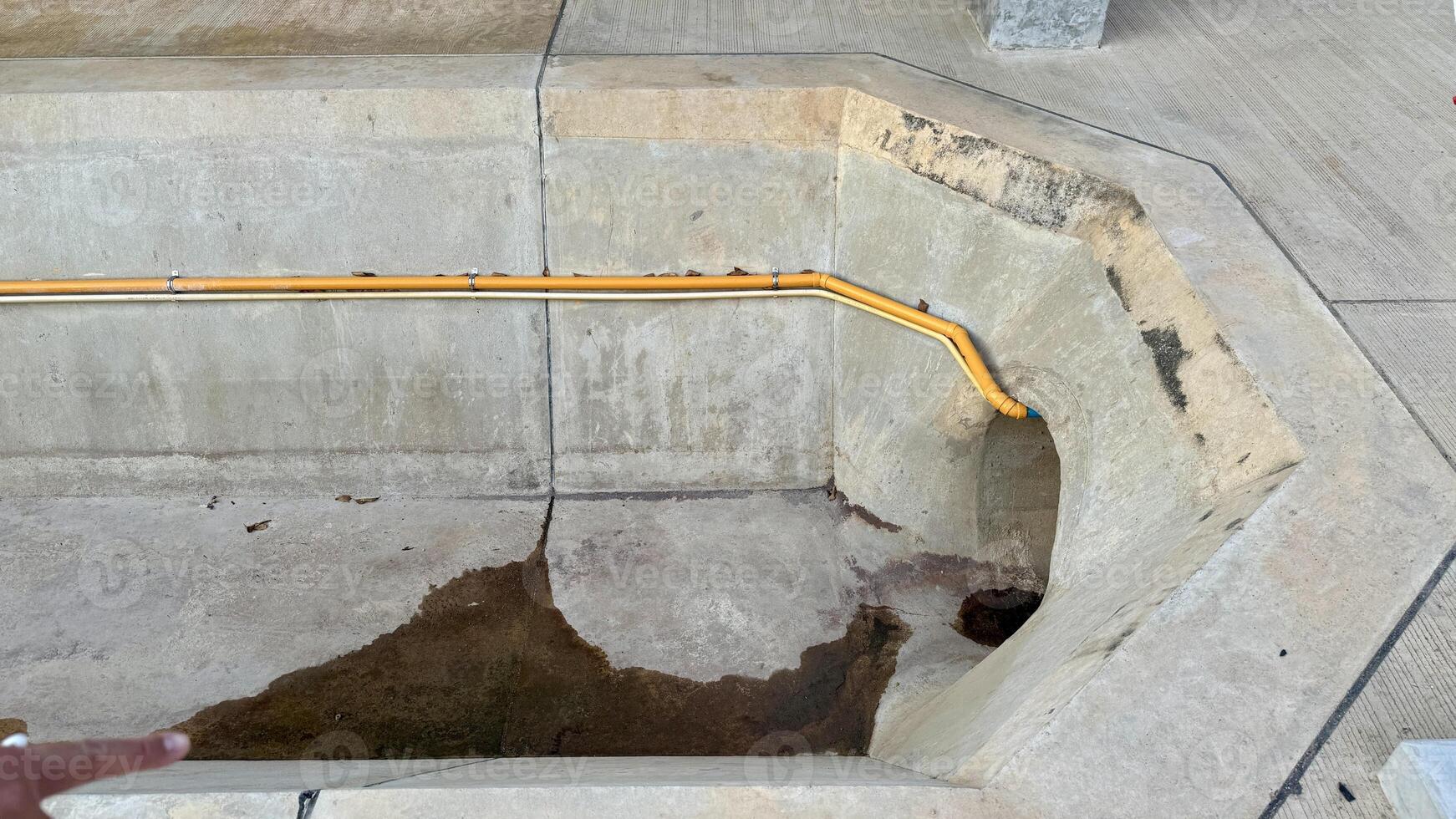 Concrete Water Feature A close-up view of a concrete water feature with a yellow pipe. The water feature is rectangular and has a curved edge. photo