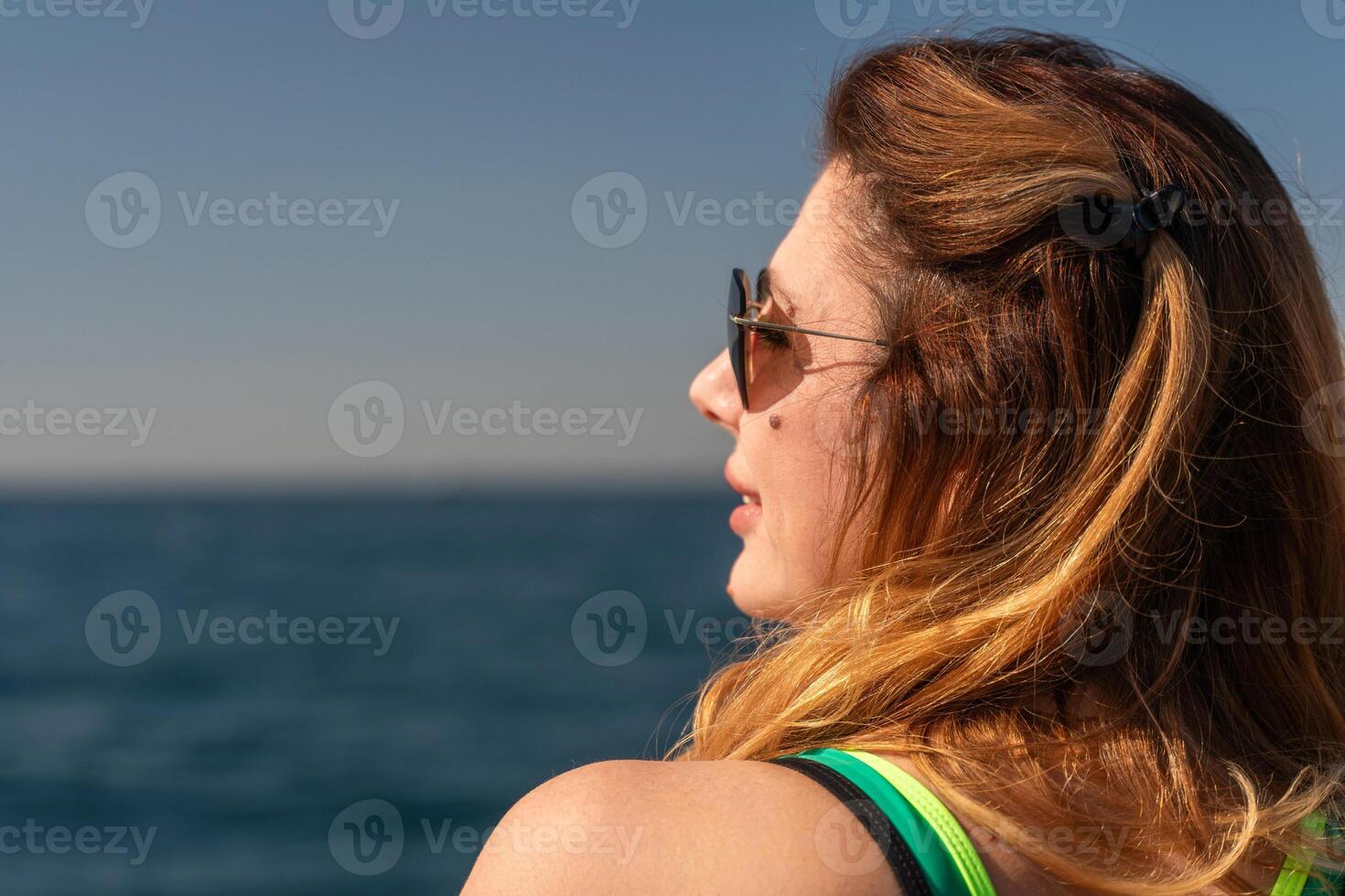 Woman Sunglasses Ocean - A woman with sunglasses looks out over a vast ocean on a sunny day. photo
