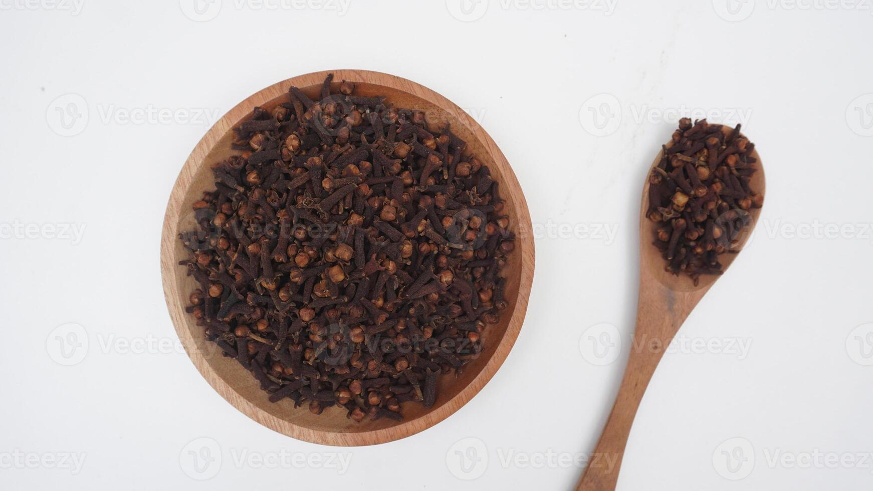 Top View of Dried Cloves on Wooden Plate and Spoon with Selective Focus on White Background photo