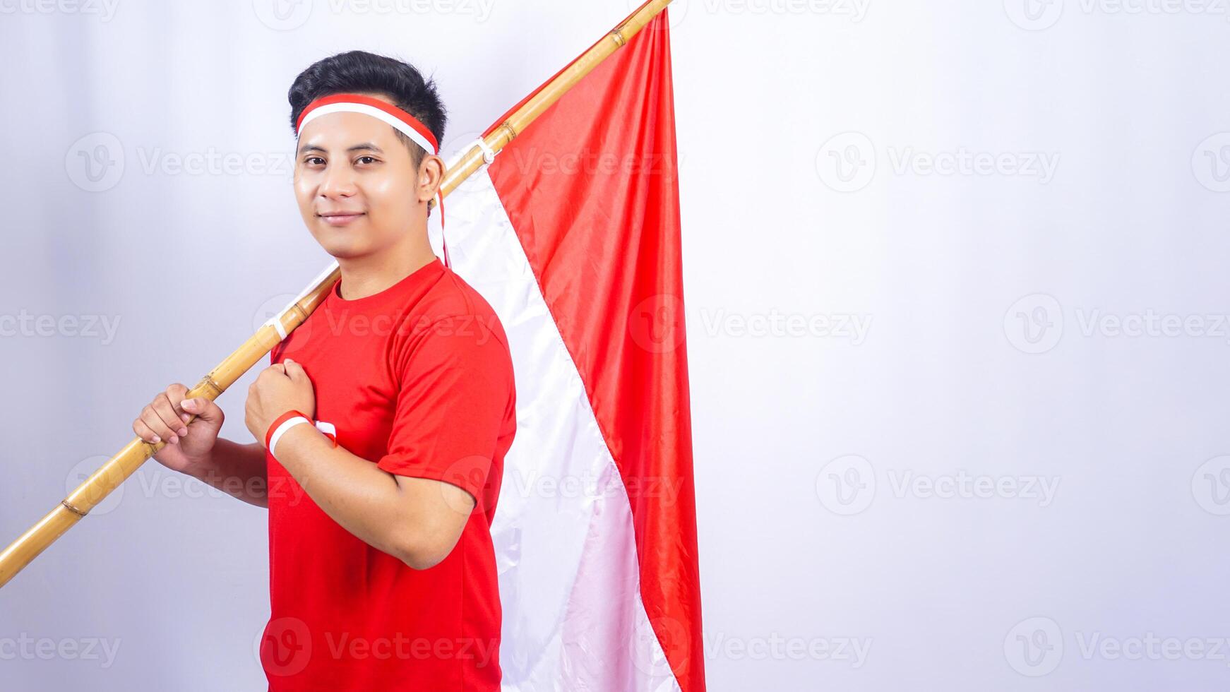 Portrait of Indonesian Man with Red and White Flag Showing Salute Pose on White Background photo