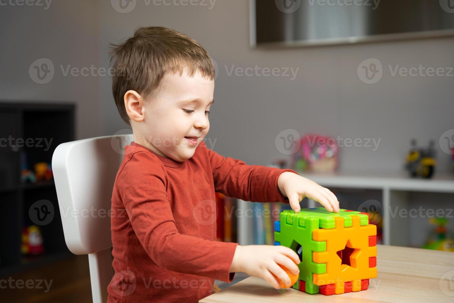 A cute happy little toddler boy of two years old sits at a children's table and plays with multi-colored sorter. Educational logic toys for children. Soft selective focus photo