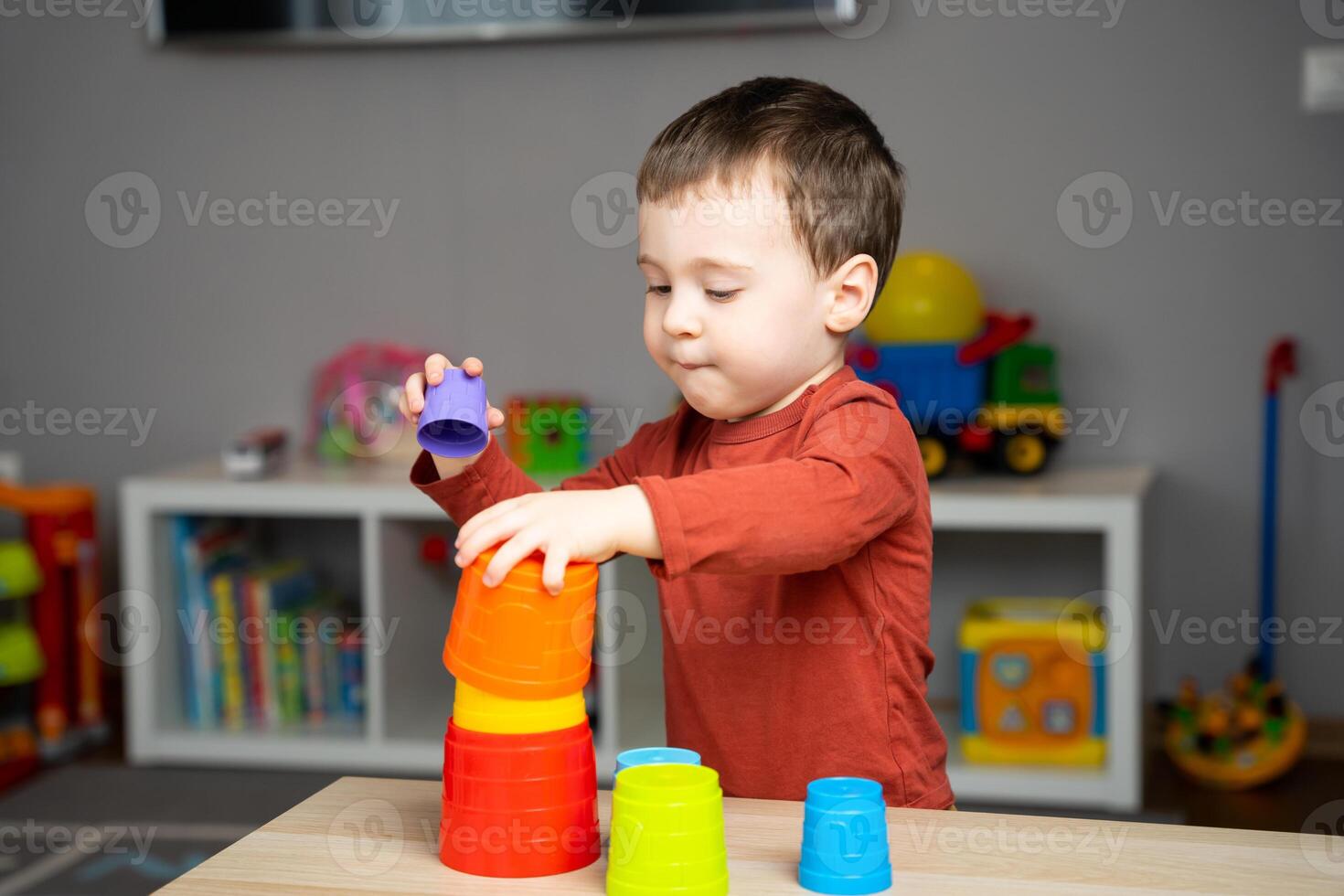 A cute happy little toddler boy of two years old sits at a children's table and plays with multi-colored pyramids in his room. Educational toys for children. Soft photo