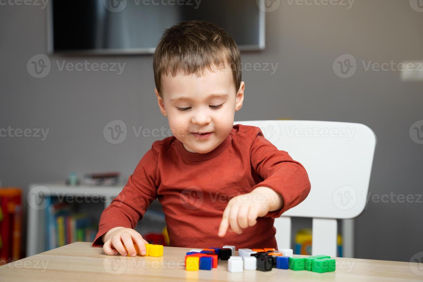 A cute happy little toddler boy of two years old sits at a children's table and plays with multi-colored blocks in his room. Educational toys for children. Soft selective focus photo
