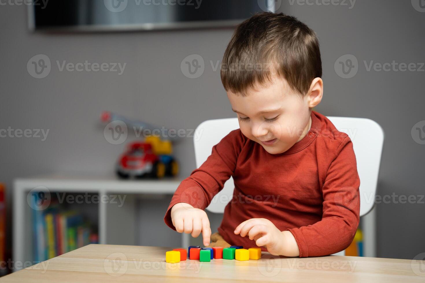 A happy cute little toddler boy of two years old sits at a children's table and plays with colorful cubes. Educational logic toys for children. Soft selective focus photo