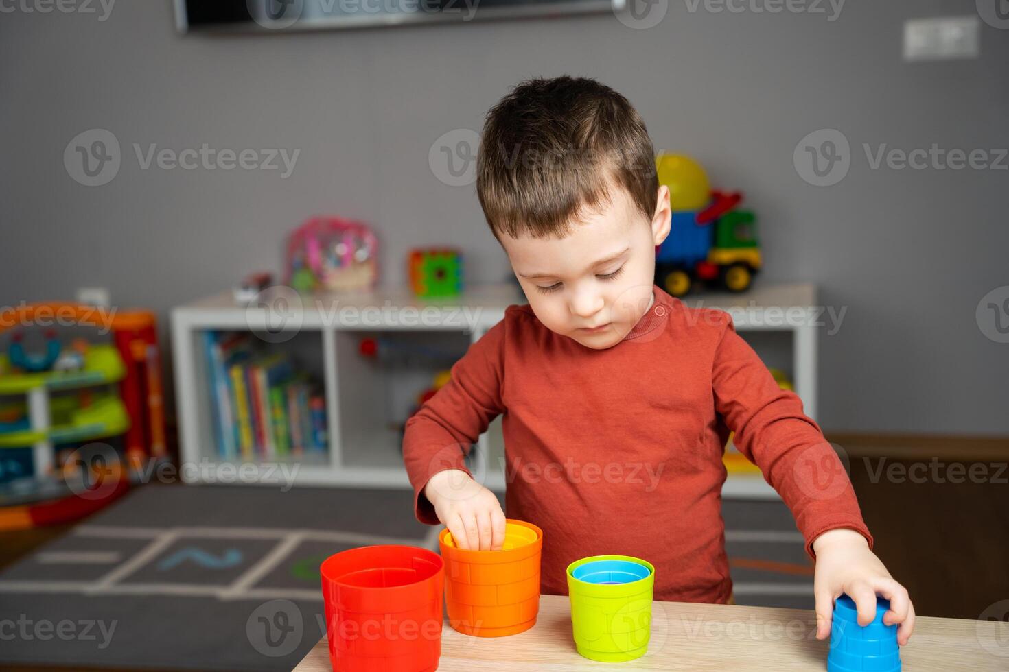 A cute happy little toddler boy of two years old sits at a children's table and plays with multi-colored pyramids in his room. Soft selective focus photo