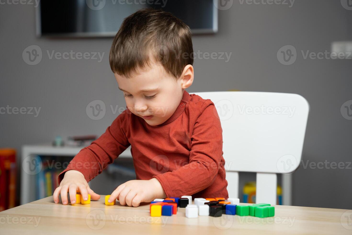 A cute little toddler boy of two years old sits at a children's table and plays with colorful cubes. Educational logic toys for children. Soft selective focus photo