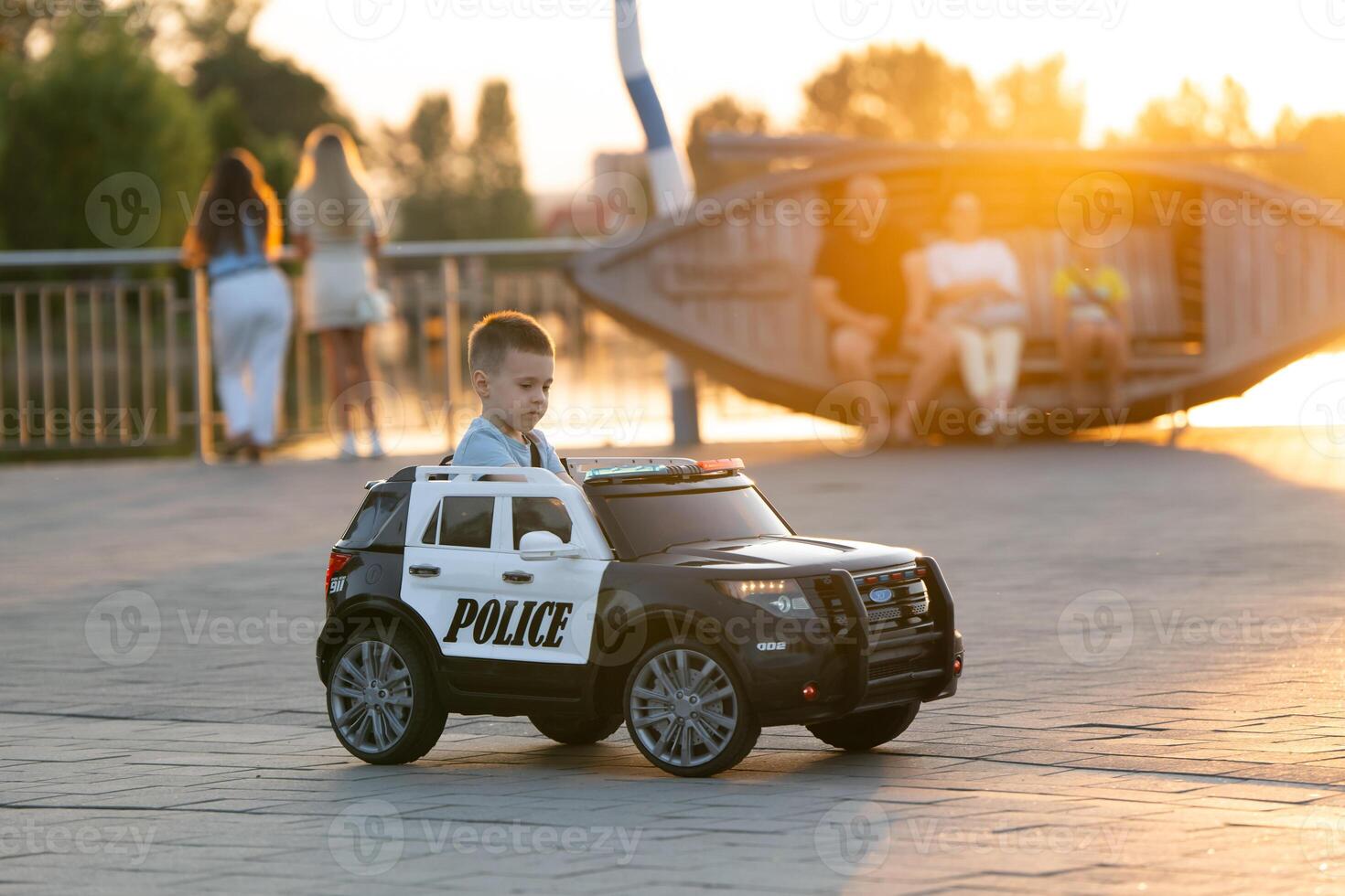 A little caucasian toddler boy of three and a half years old rides a toy car in a summer park near lake on a sunset light. Childhood and pastime. photo