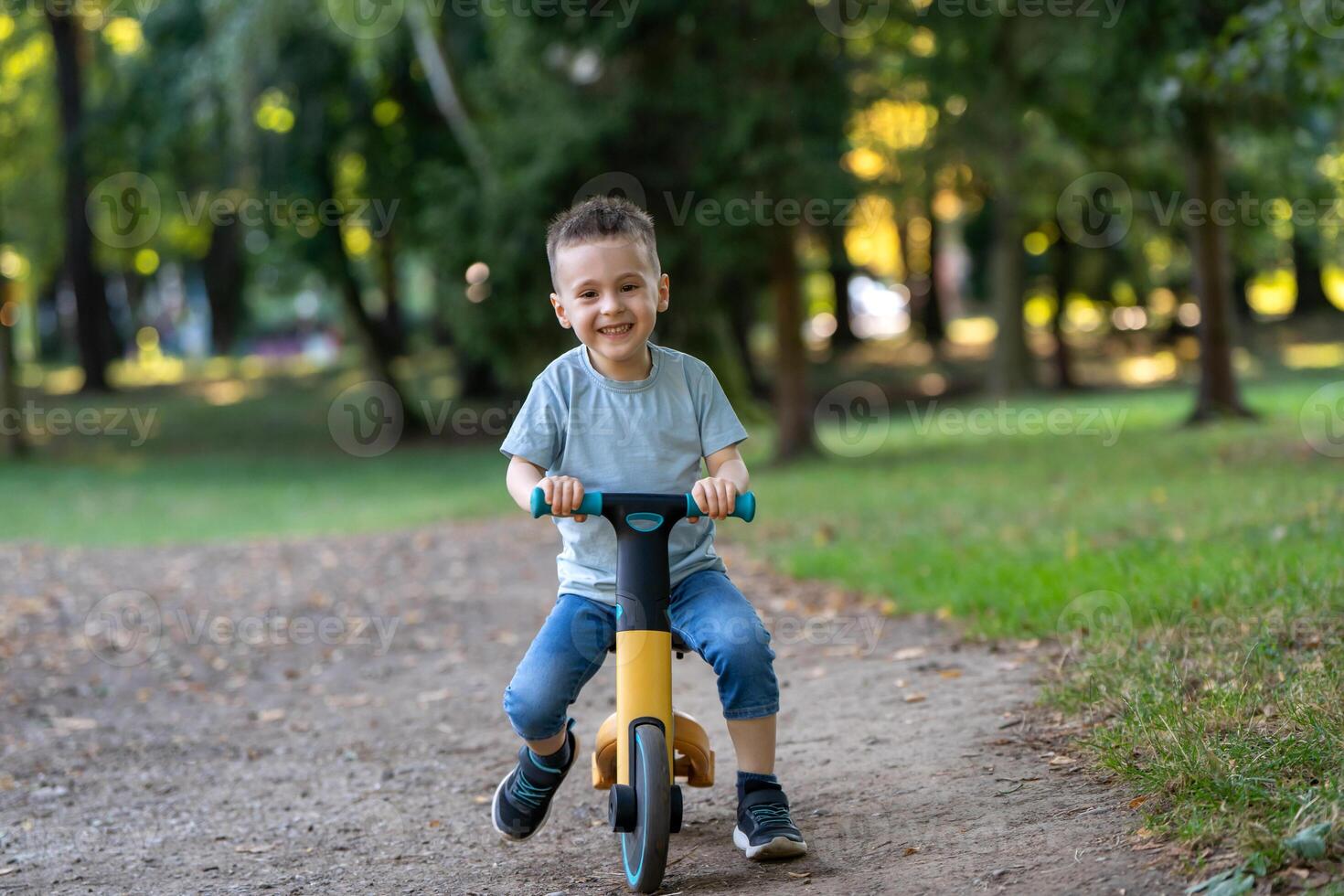 A cute smiling toddler boy of three or four years old rides a bicycle or balance bike in a city park on a sunny summer day. Toddlerhood and childhood concept photo